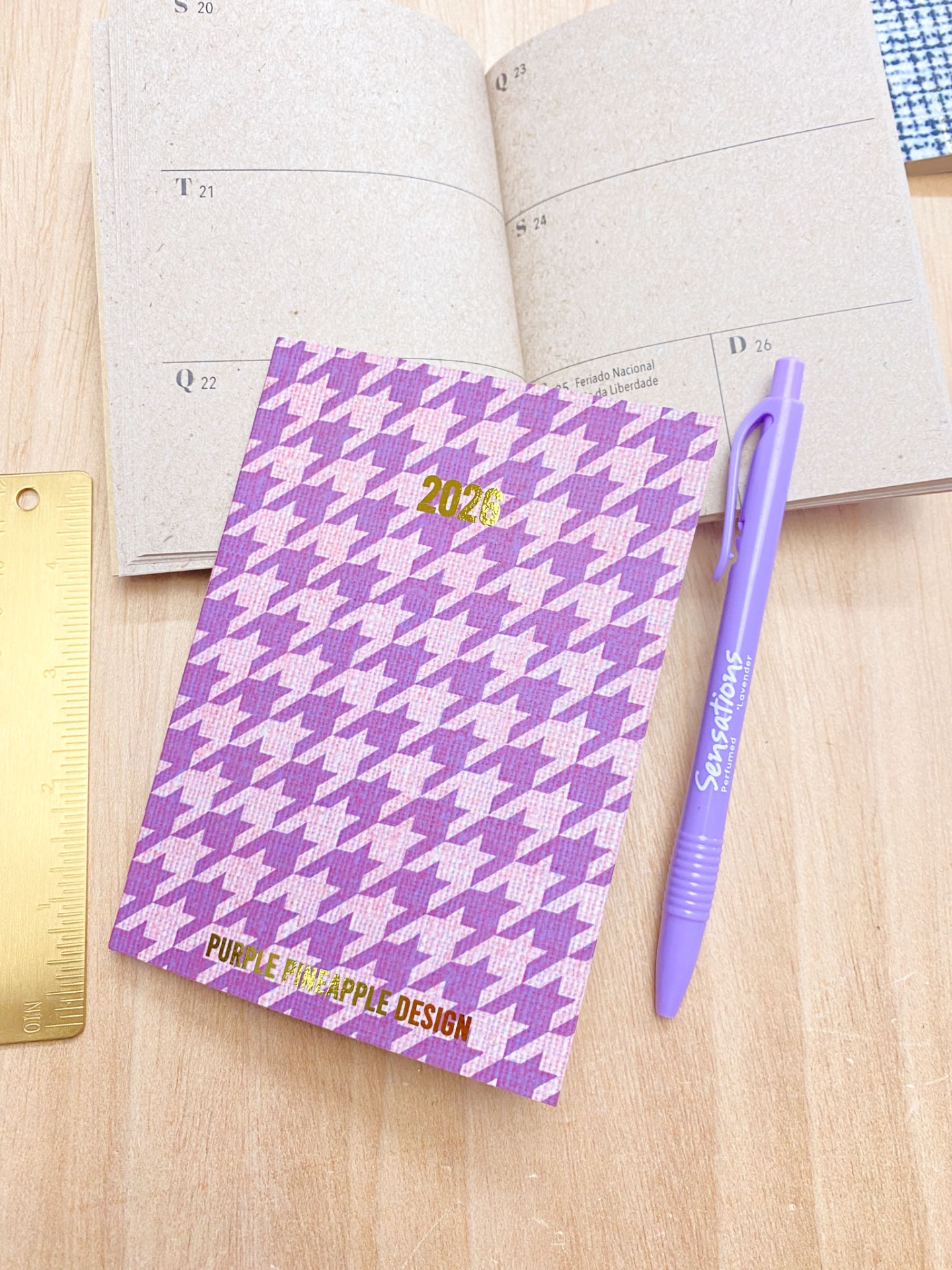 Caderno 2026 com padrão roxo, caneta roxa e régua dourada sobre mesa