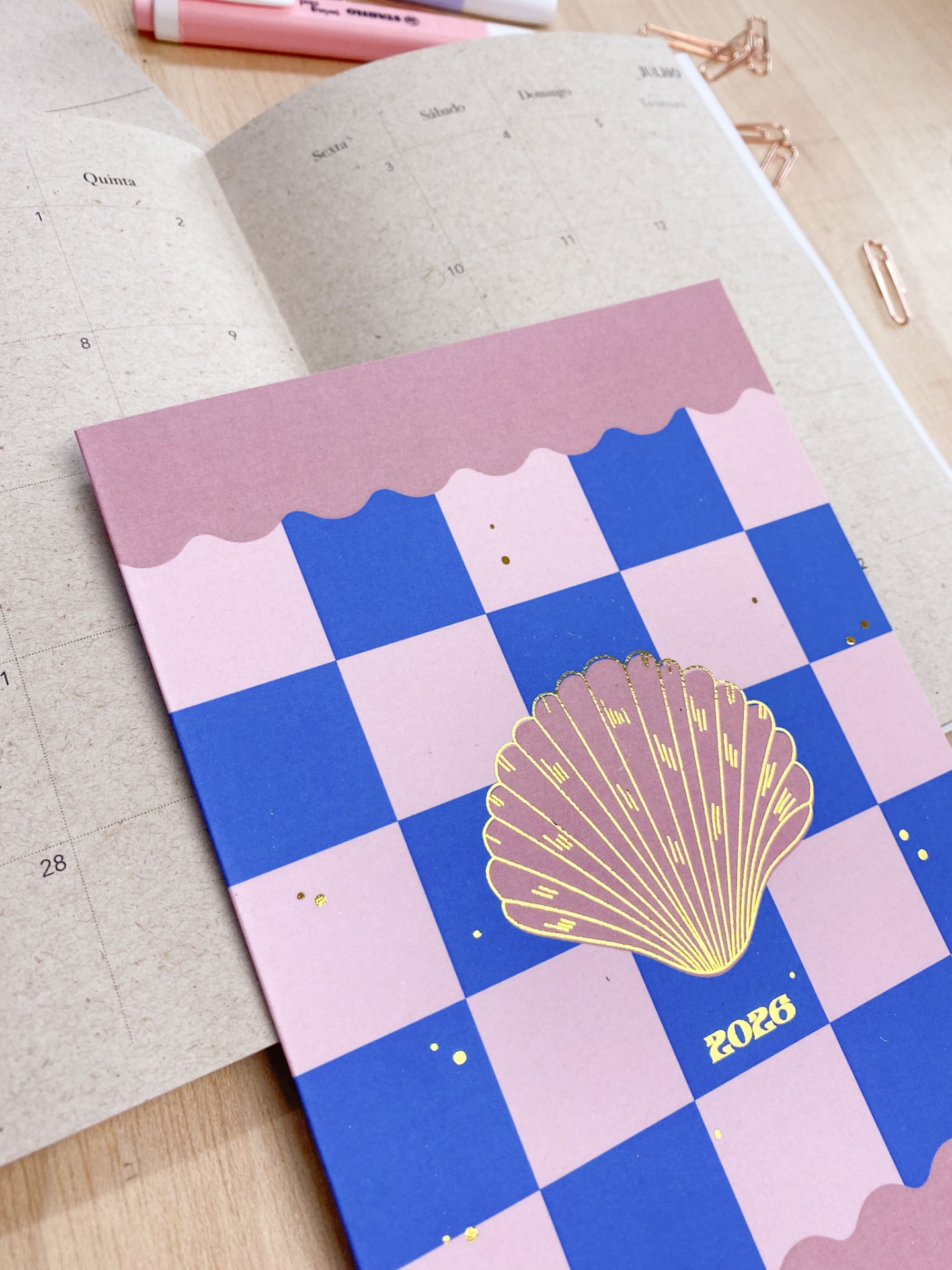 Agenda 2026 rosa e azul com concha dourada sobre mesa de madeira