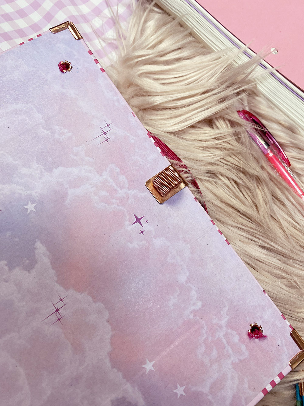 Caderno rosa com desenho de nuvens, estrelas, cantos dourados e cristais rosa