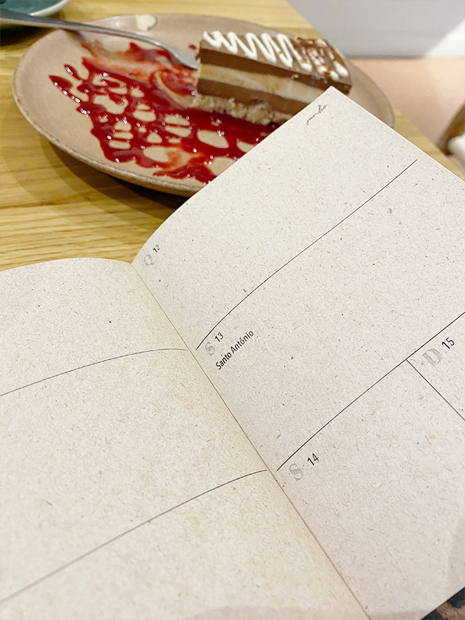 Agenda aberta numa página semanal ao lado de um prato com fatia de bolo decorado.