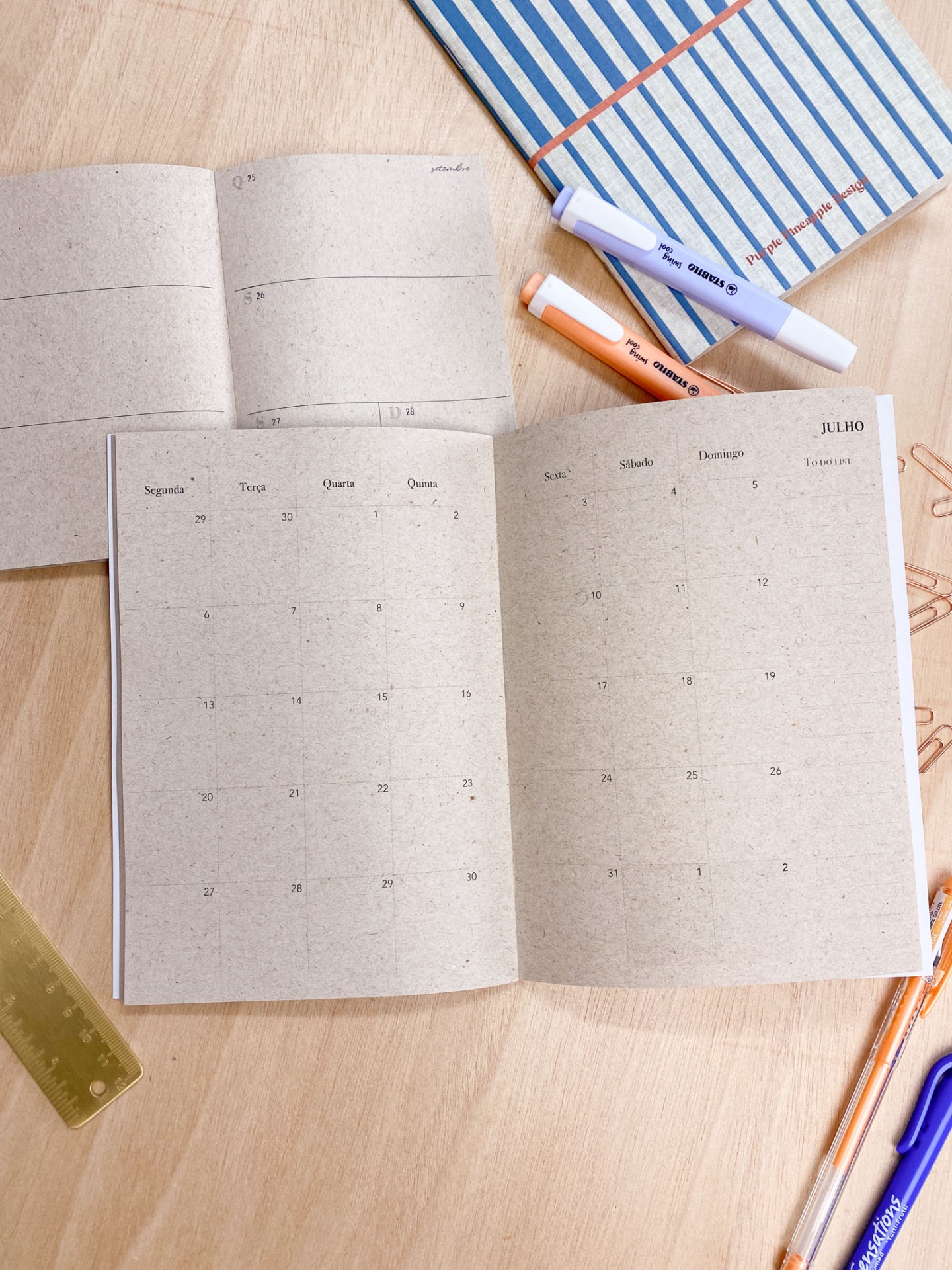 Agenda mensal aberta com papel reciclado castanho e canetas coloridas sobre mesa de madeira