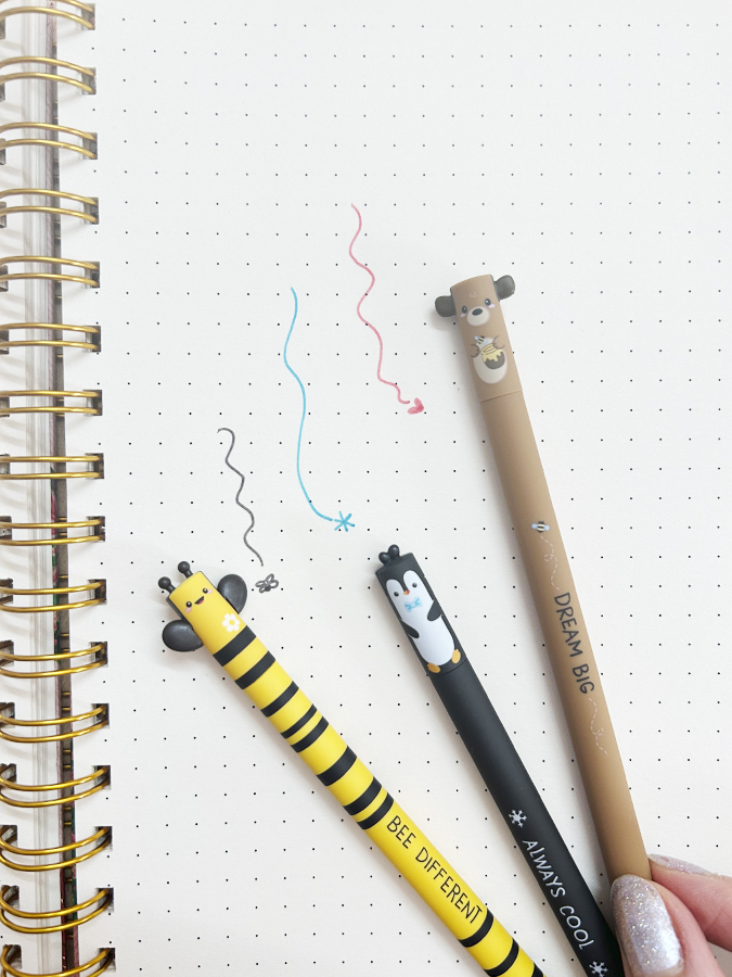Três canetas com design de animais sobre caderno com padrão de pontos
