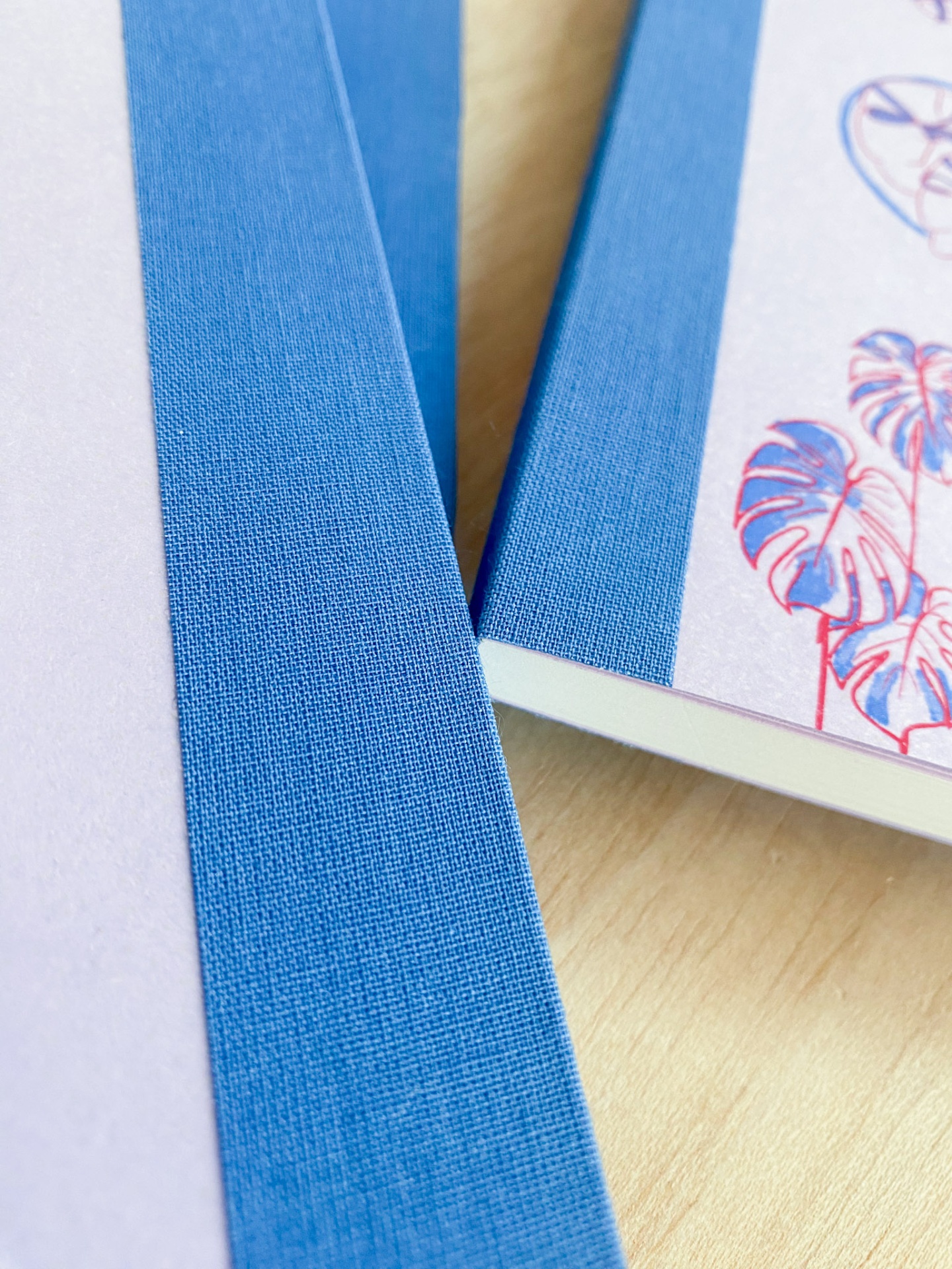 Dois cadernos com lombada azul e capa floral sobre mesa de madeira clara