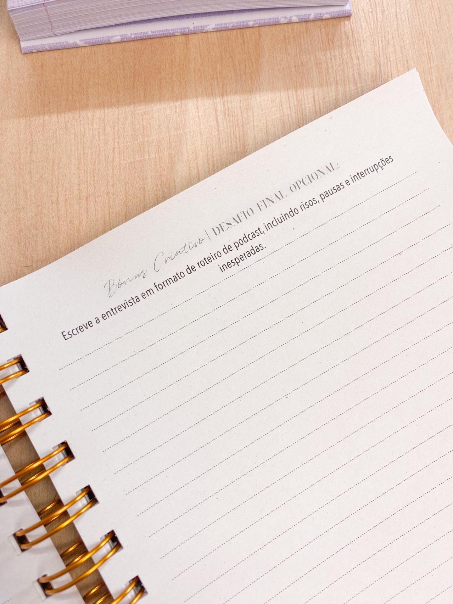 Página de caderno aberto com linhas e texto em português no topo, sobre mesa de madeira clara.