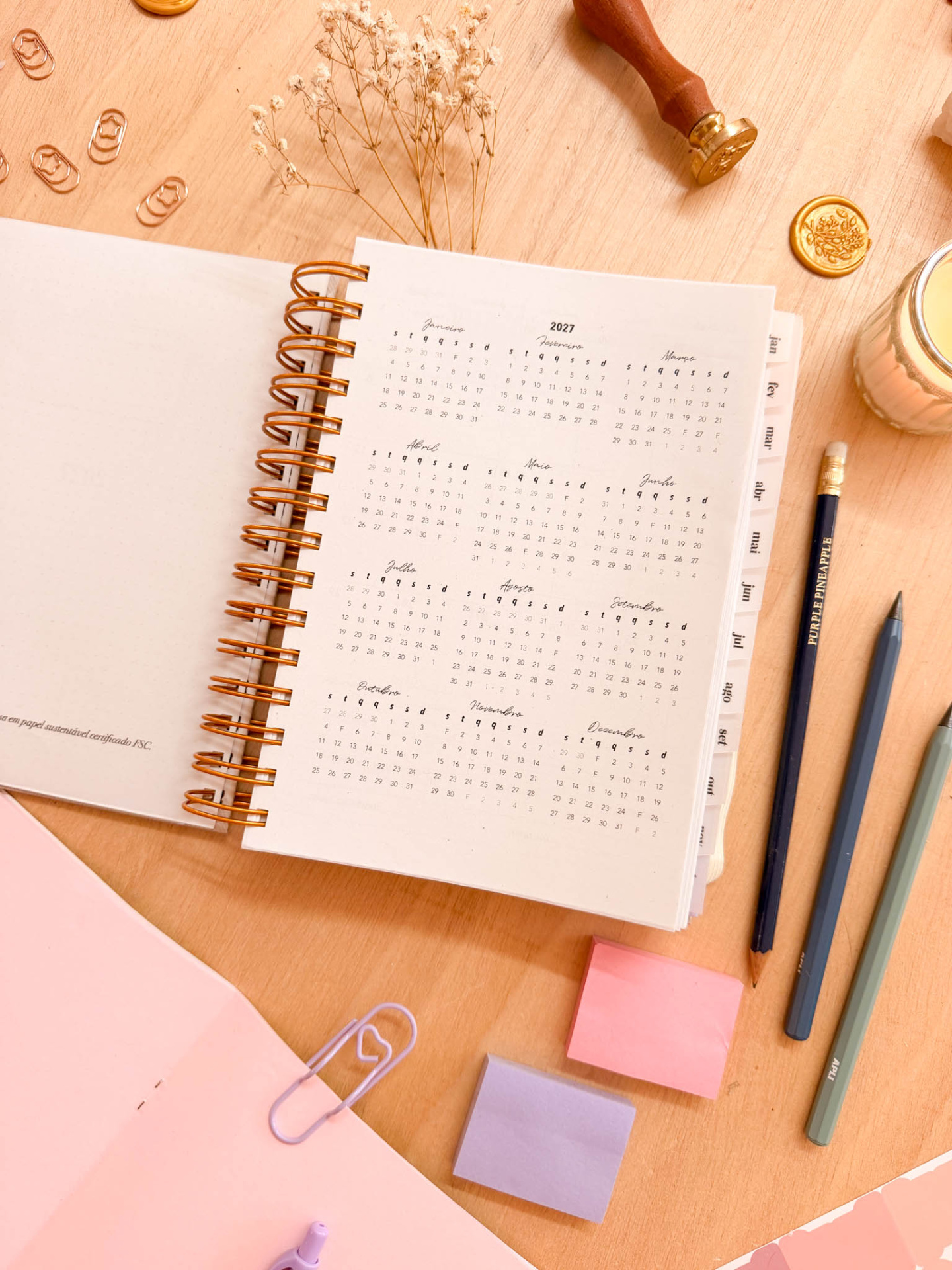 Agenda espiral com calendário 2027 e acessórios de escritório sobre mesa de madeira