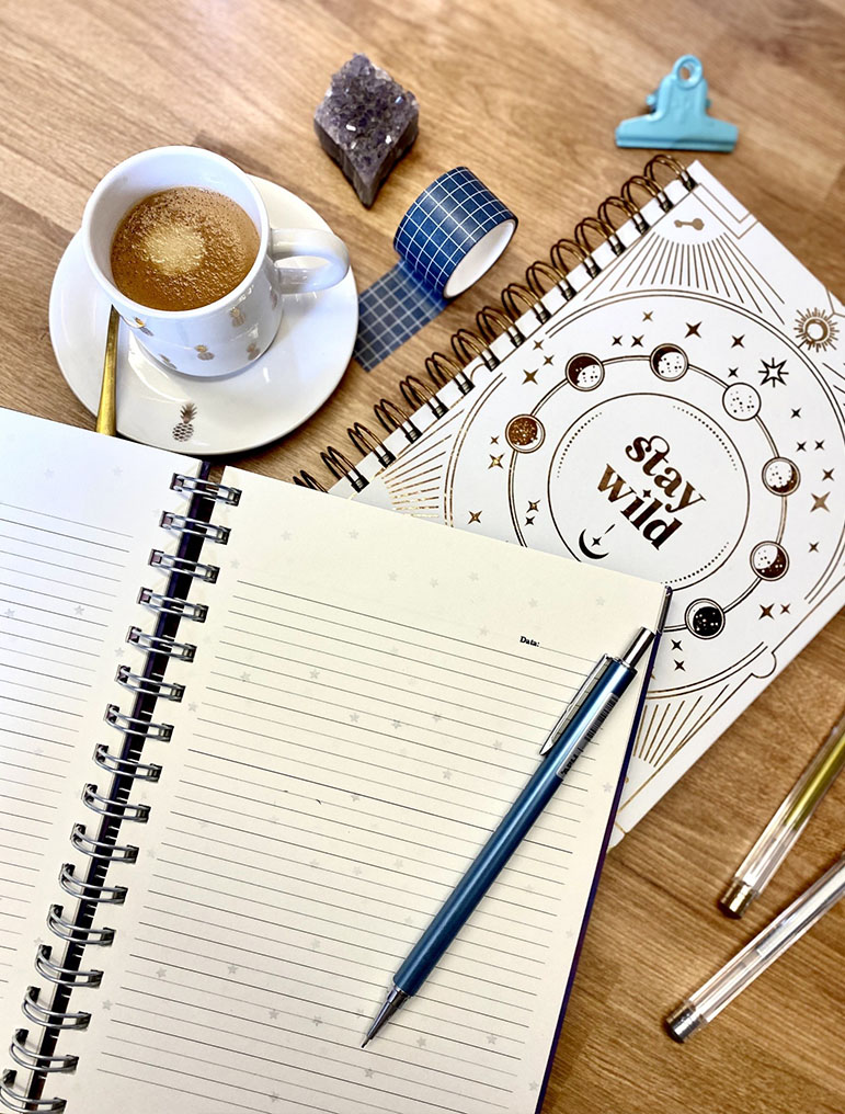 Mesa com chávena de café, bloco de notas, caneta, fita adesiva azul, pedra ametista e bloco com capa 'stay wild'