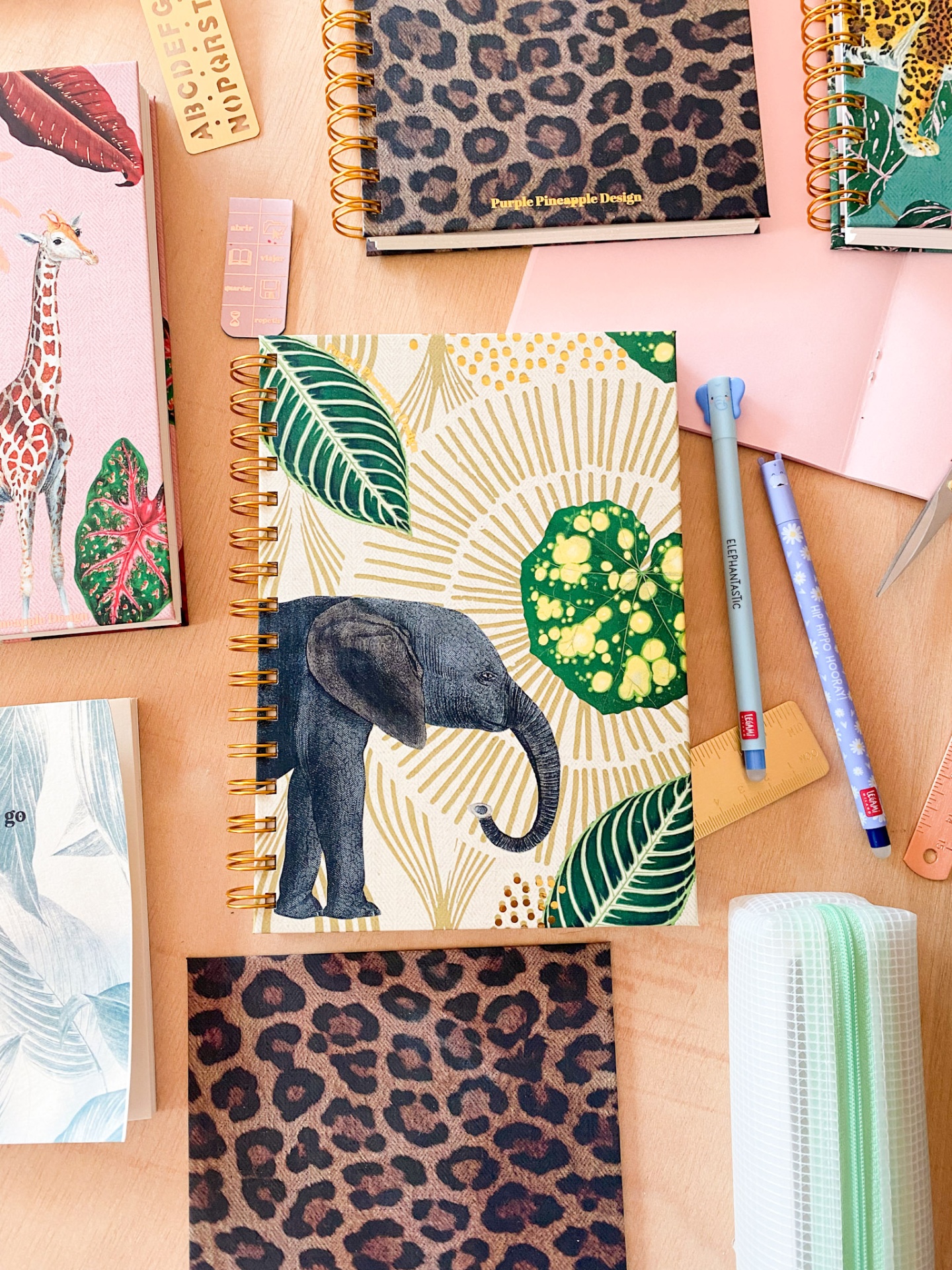 Cadernos espiral com várias capas coloridas e padrões variados sobre mesa de madeira com material escolar