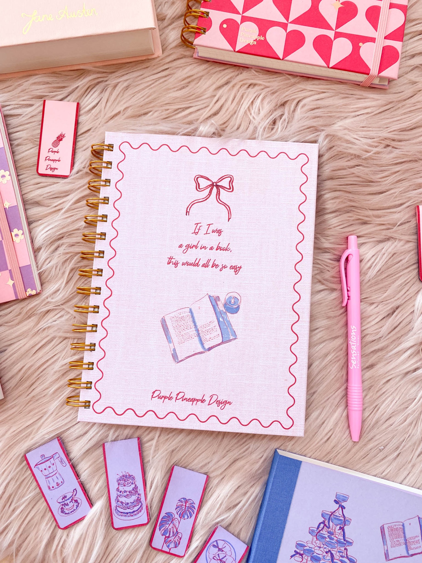 Caderno espiral branco com desenho e texto, caneta cor-de-rosa e marcadores de página em superfície felpuda