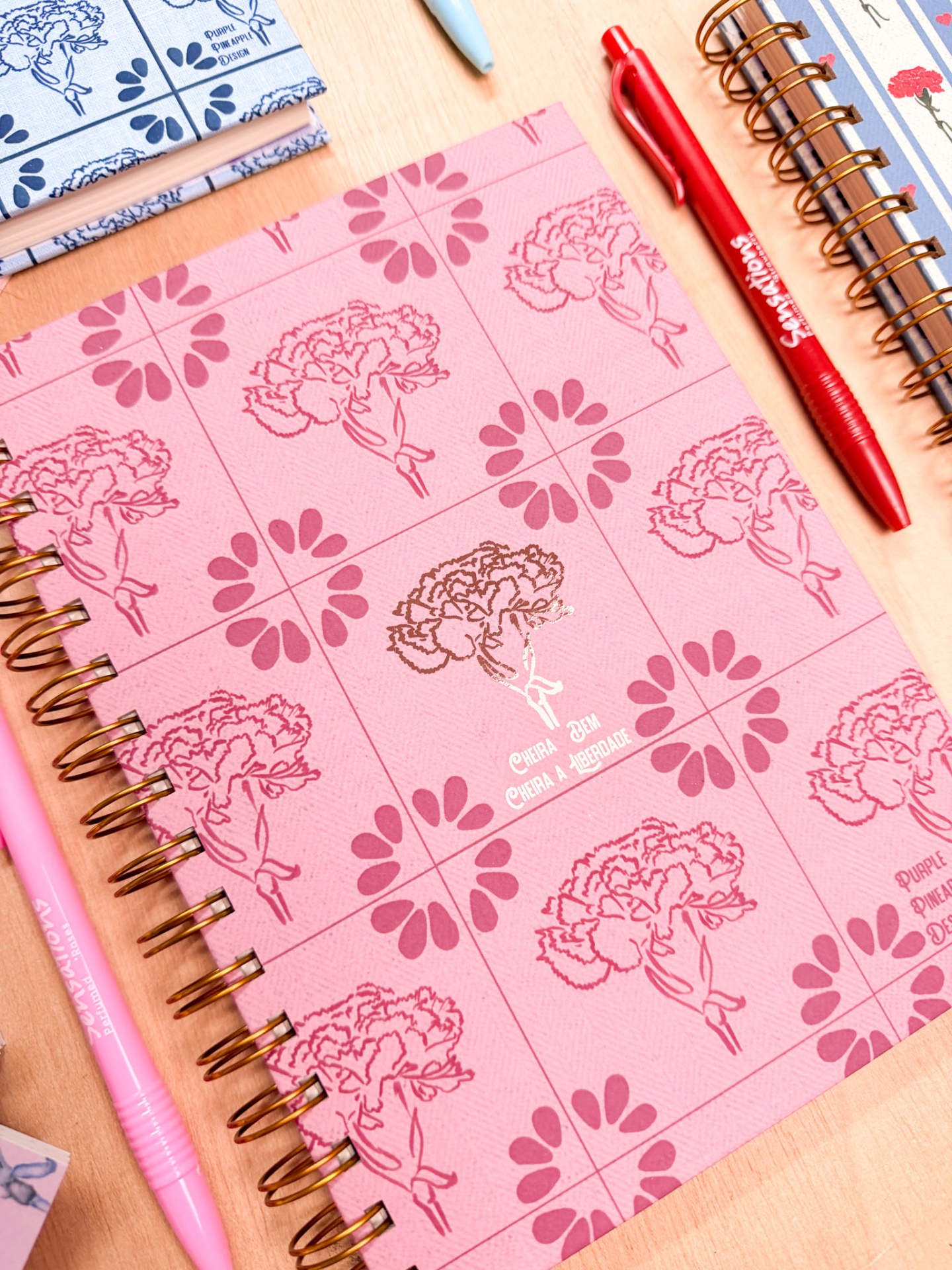 Cadernos espiralados com capas decoradas de flores e canetas coloridas sobre mesa de madeira