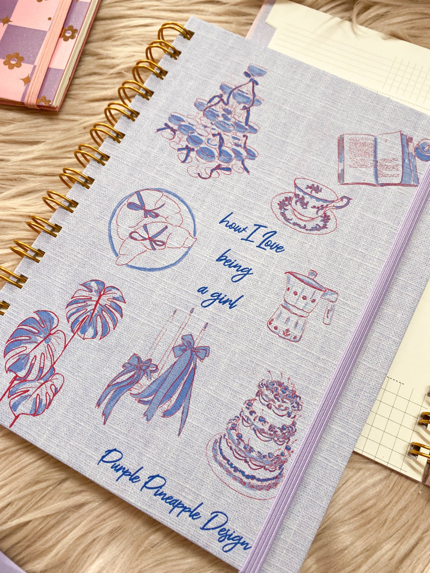 Agenda ou caderno com capa cinzenta decorada com desenhos roxos e texto azul.