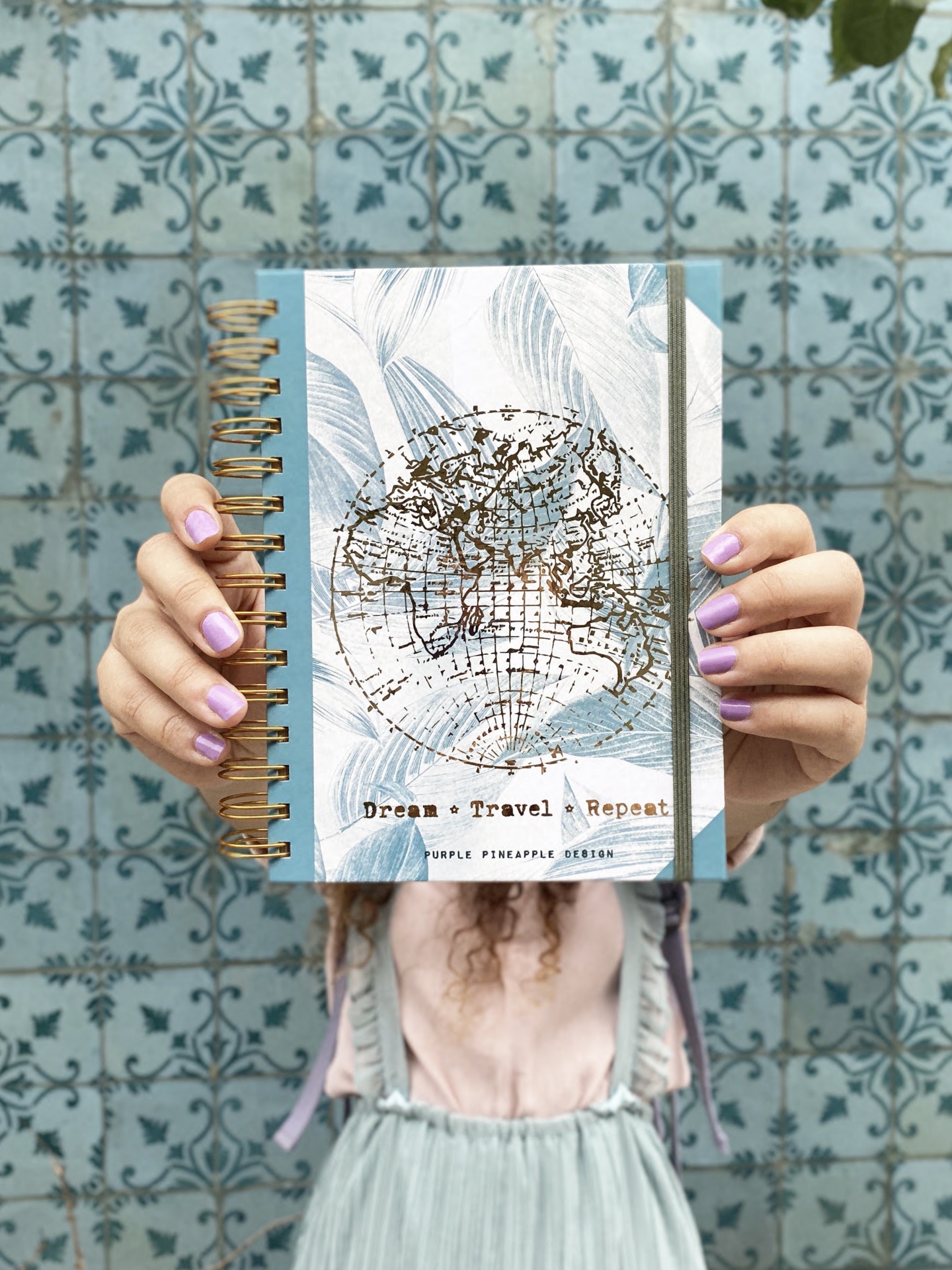 Caderno espiral com capa decorada com mapa e texto, em fundo de azulejos azuis