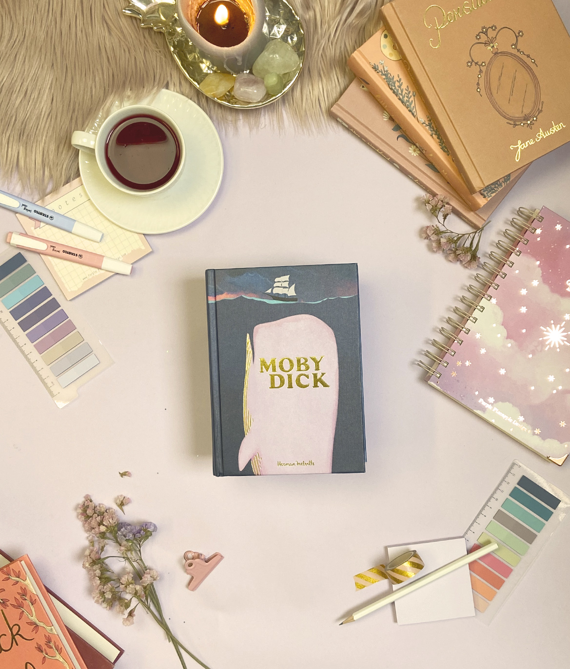 Livro Moby Dick com chá, caderno rosa, amostras de cor e vela acesa