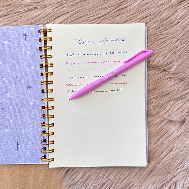 Caderno lilás com estrelas brancas aberto sobre superfície macia com caneta rosa em cima