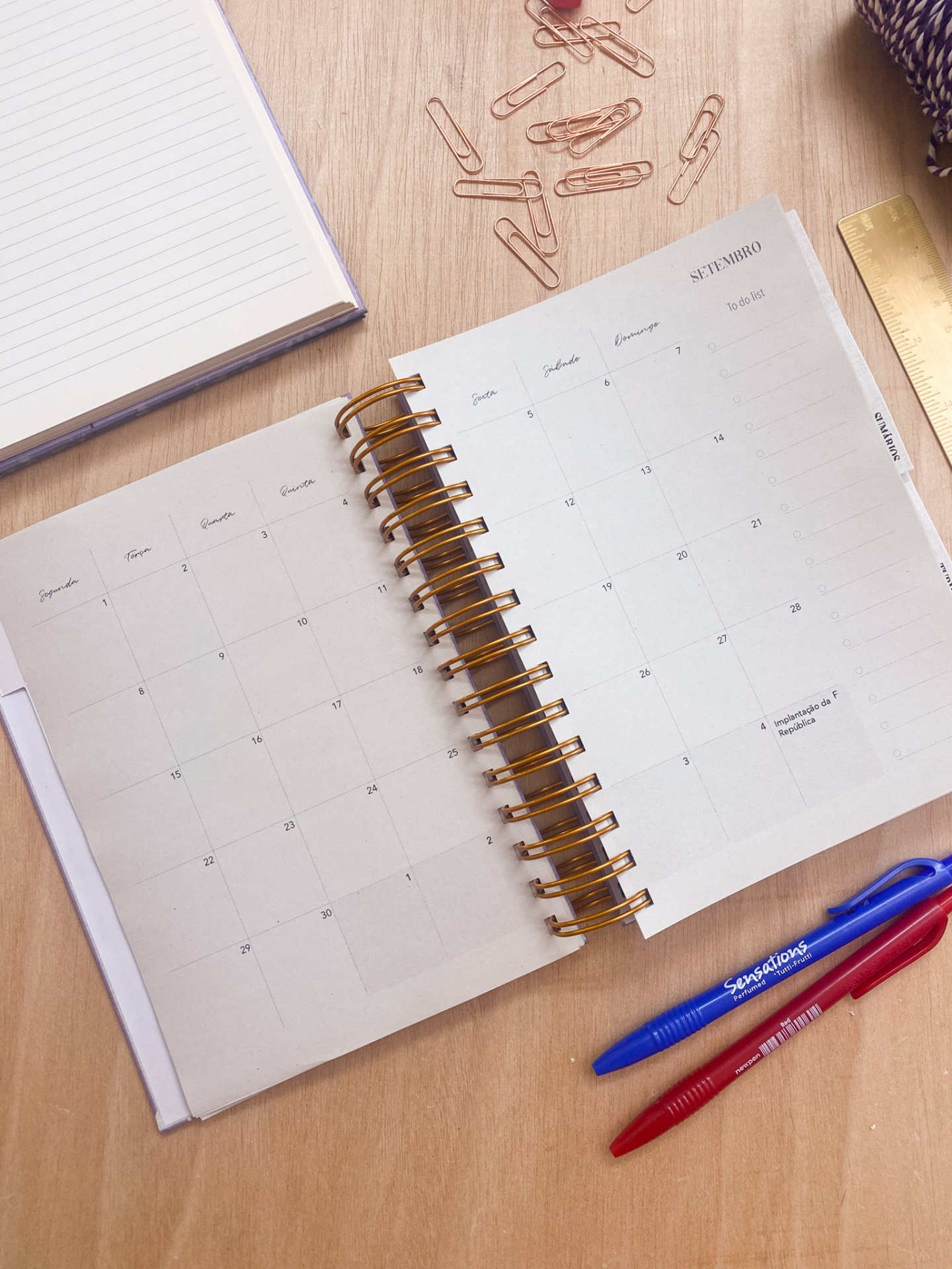 Agenda aberta com calendário de setembro de 2023 numa mesa de madeira com canetas, clips, régua e caderno