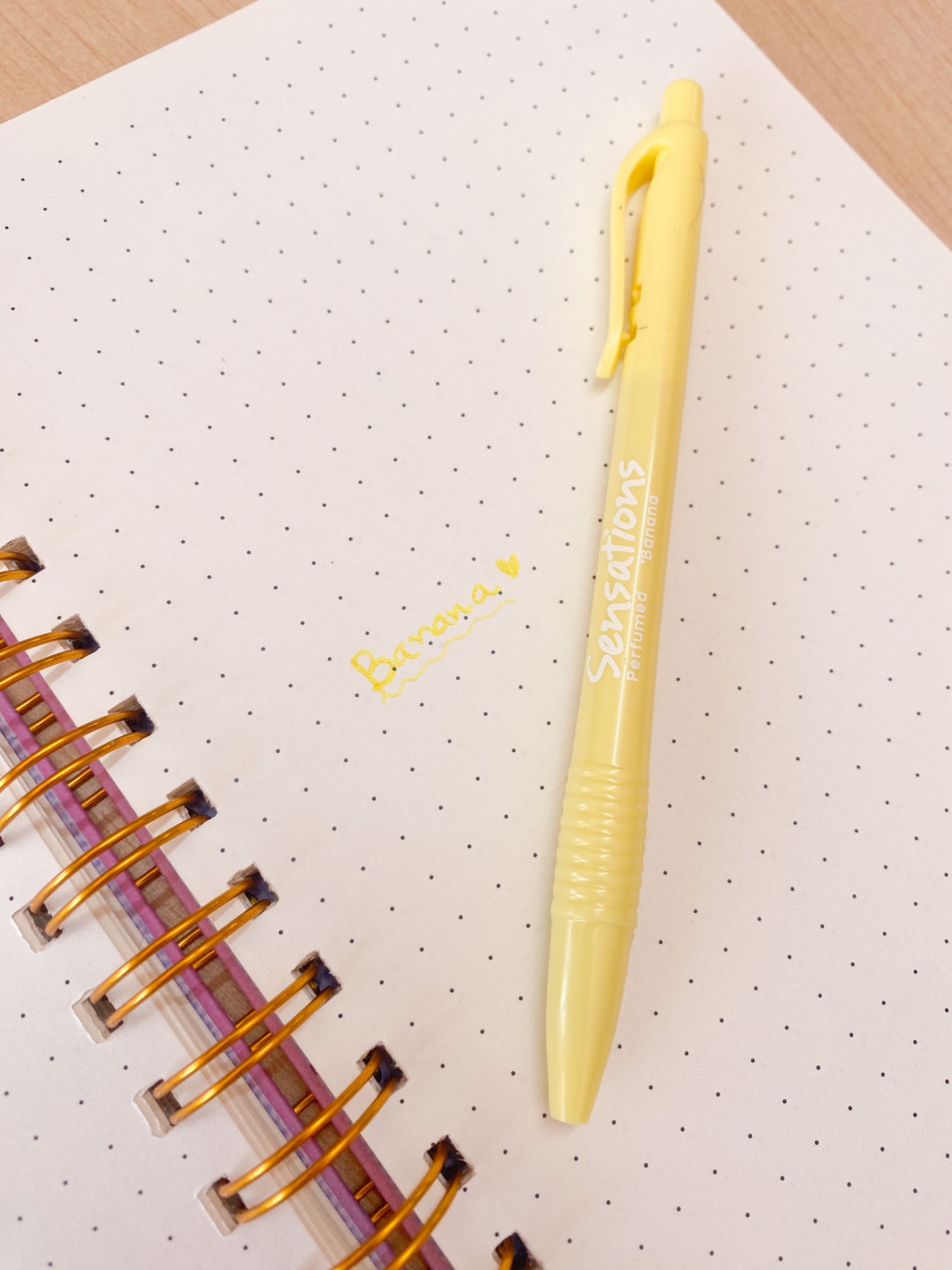Caneta amarela sobre caderno de espiral com folhas brancas e escrita amarela