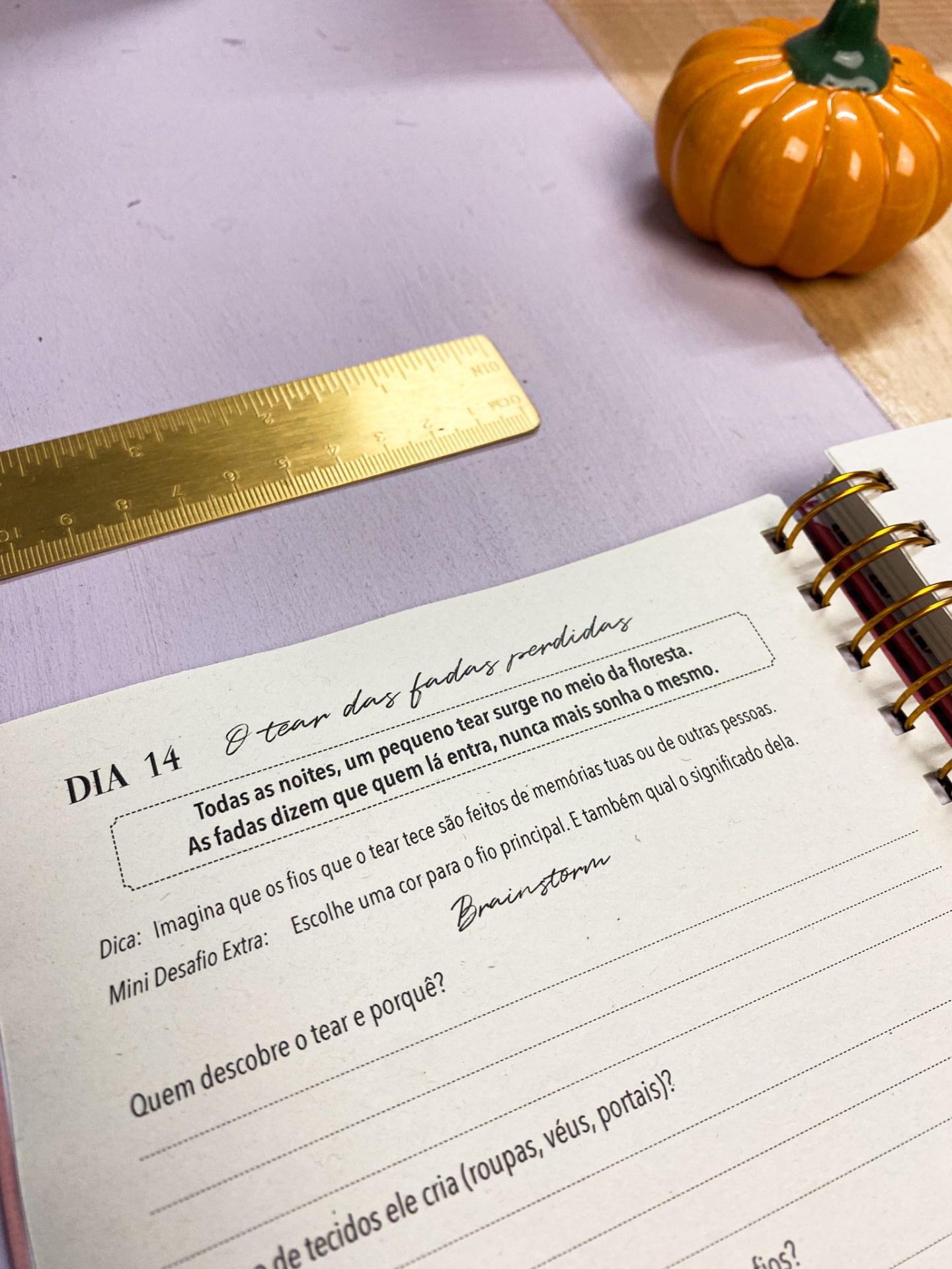 Caderno aberto com texto em português, régua metálica dourada e abóbora decorativa