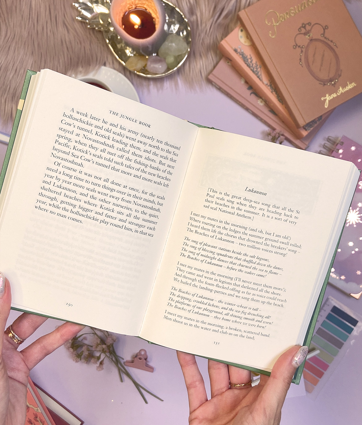 Livro aberto com texto em inglês, vela acesa e itens de papelaria sobre fundo felpudo