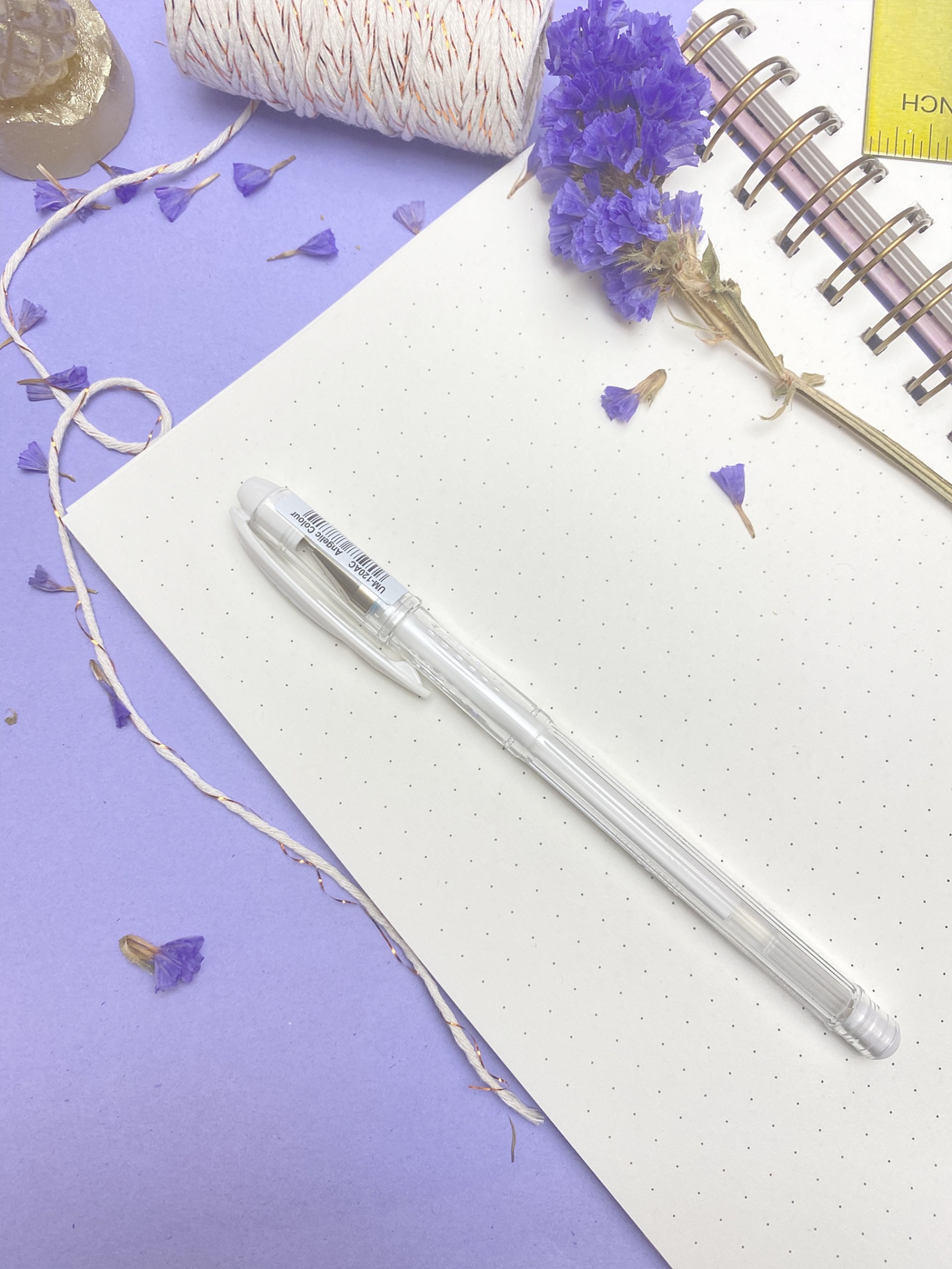 caneta branca transparente sobre folha pontilhada com flores secas e caderno espiral