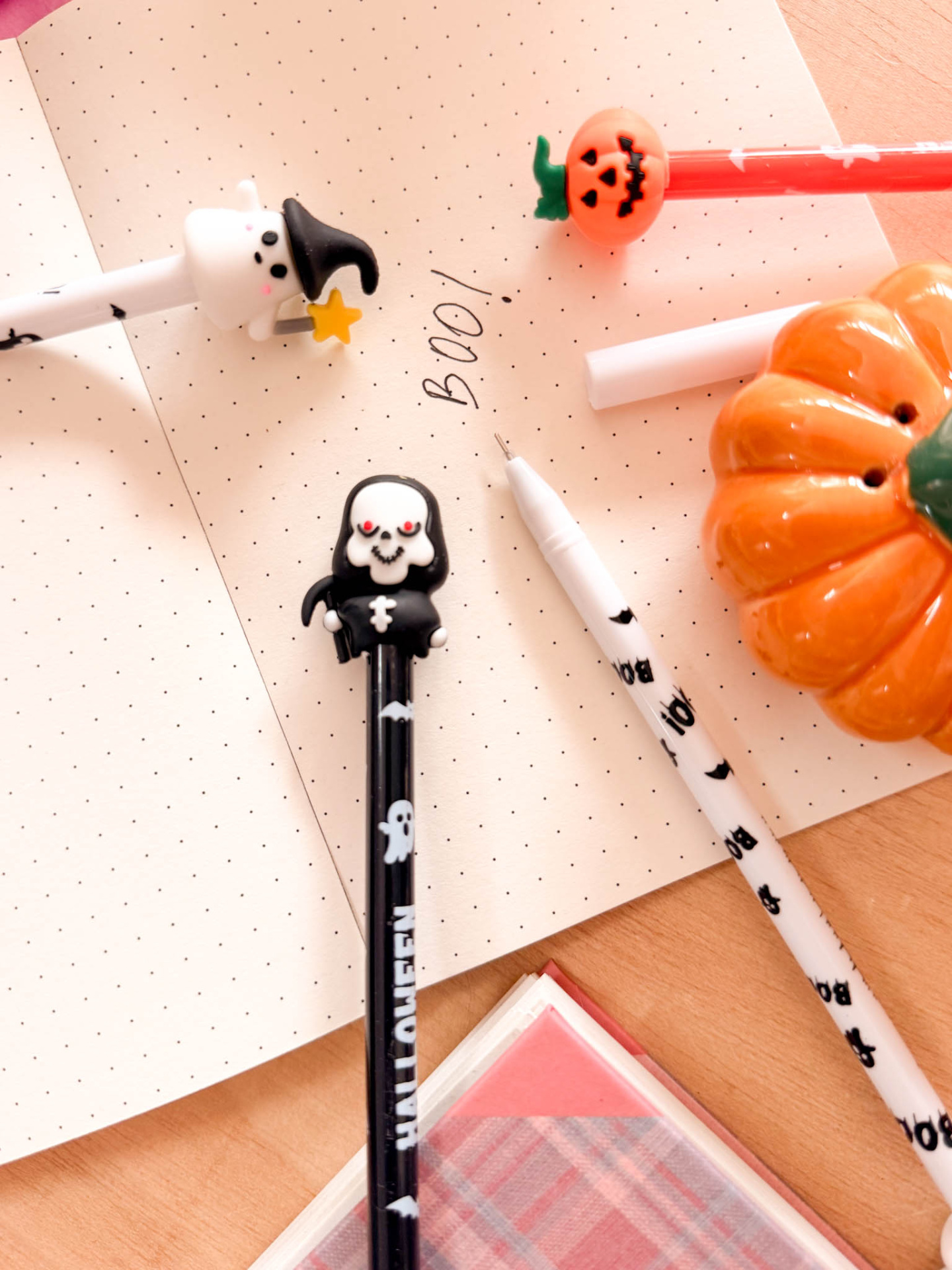 Canetas decorativas de Halloween com fantasma, caveira e abóbora numa mesa com caderno