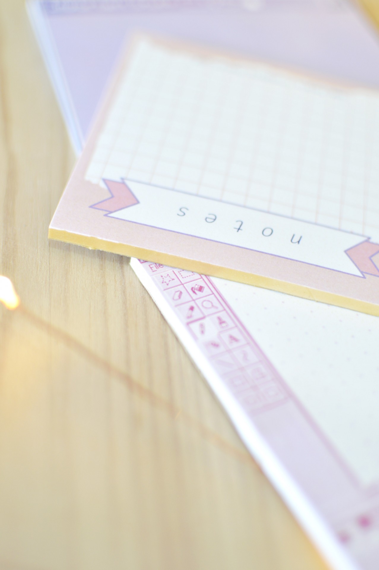 Blocos de notas com padrões de quadrícula e pontilhado em cores pastel sobre madeira clara