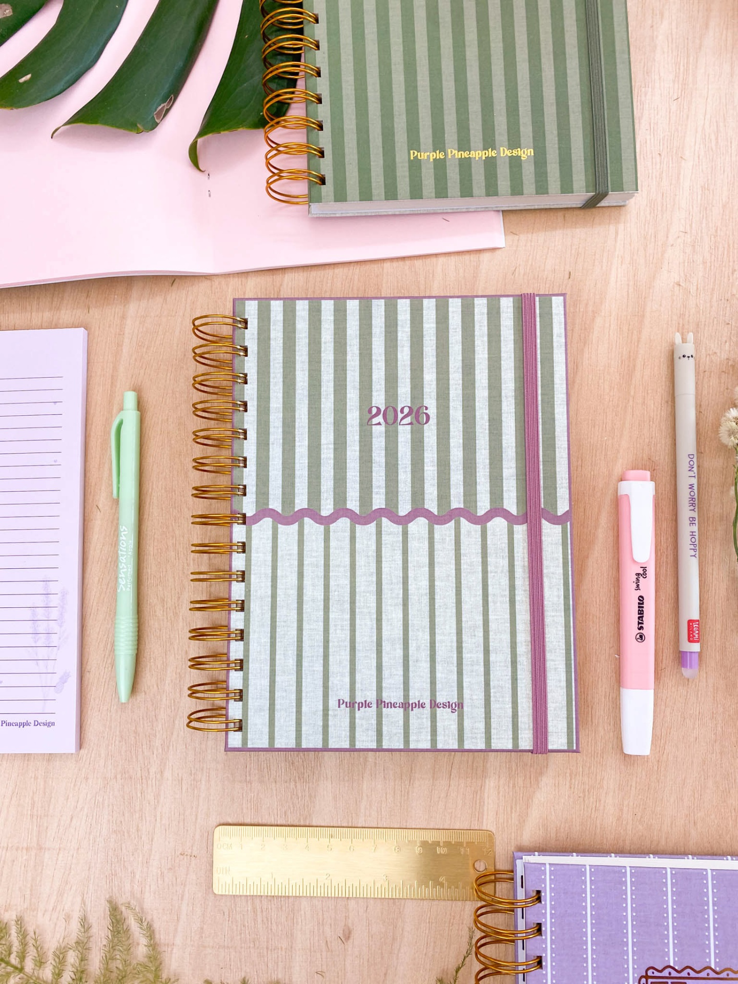 Cadernos riscado verde com canetas e régua numa mesa de madeira