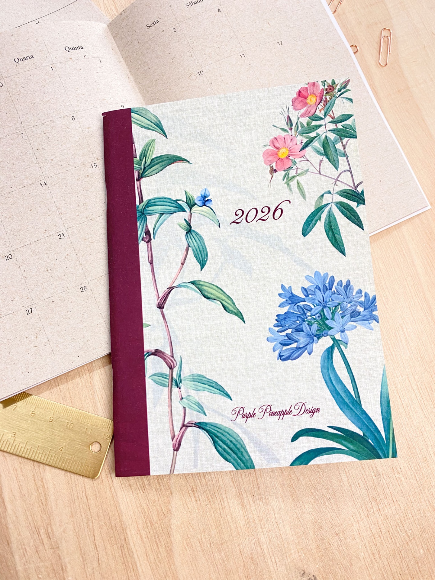 Caderno floral 2026 com capa tecido e lombada bordeaux sobre mesa de madeira