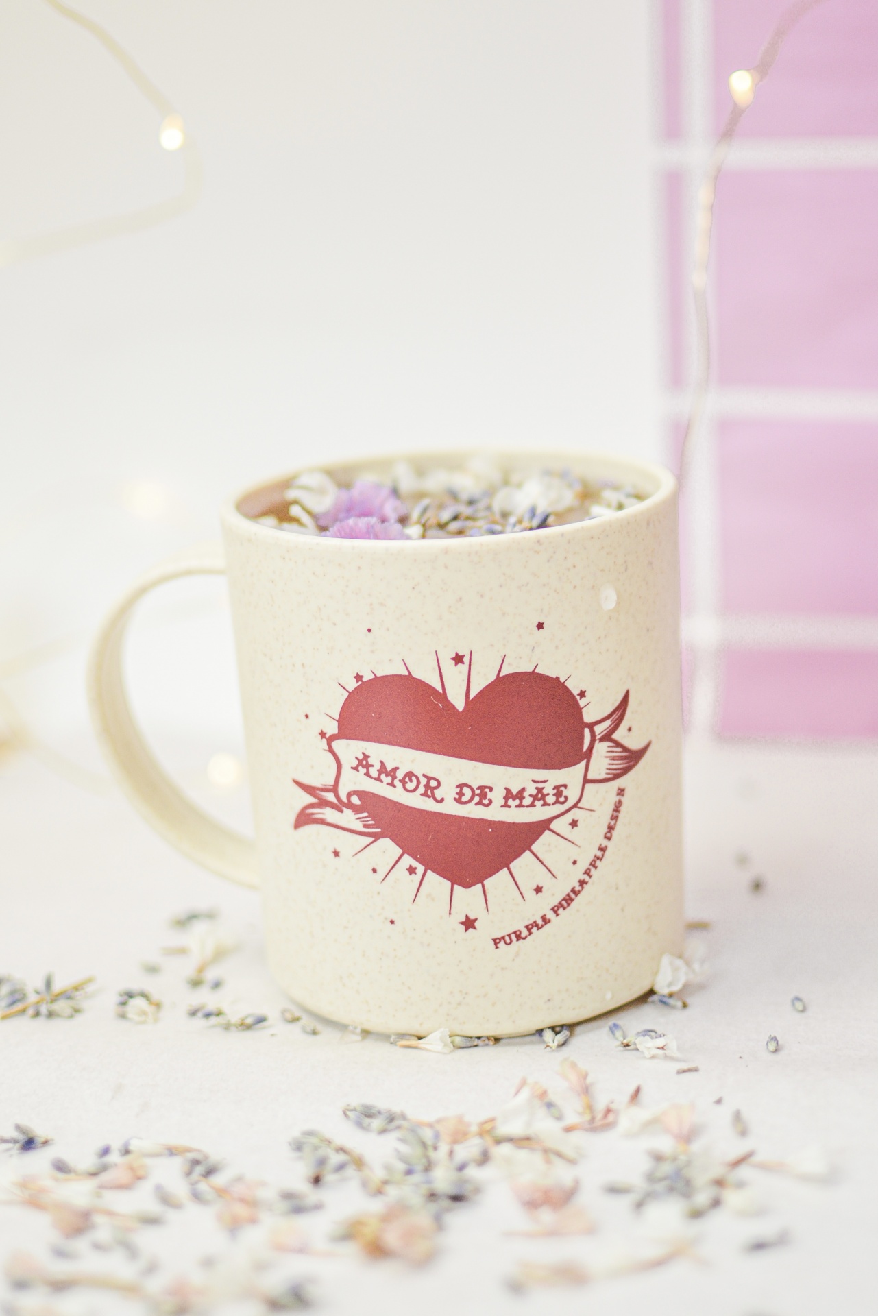 Caneca bege com coração vermelho e texto 'AMOR DE MÃE', bebida com flores secas