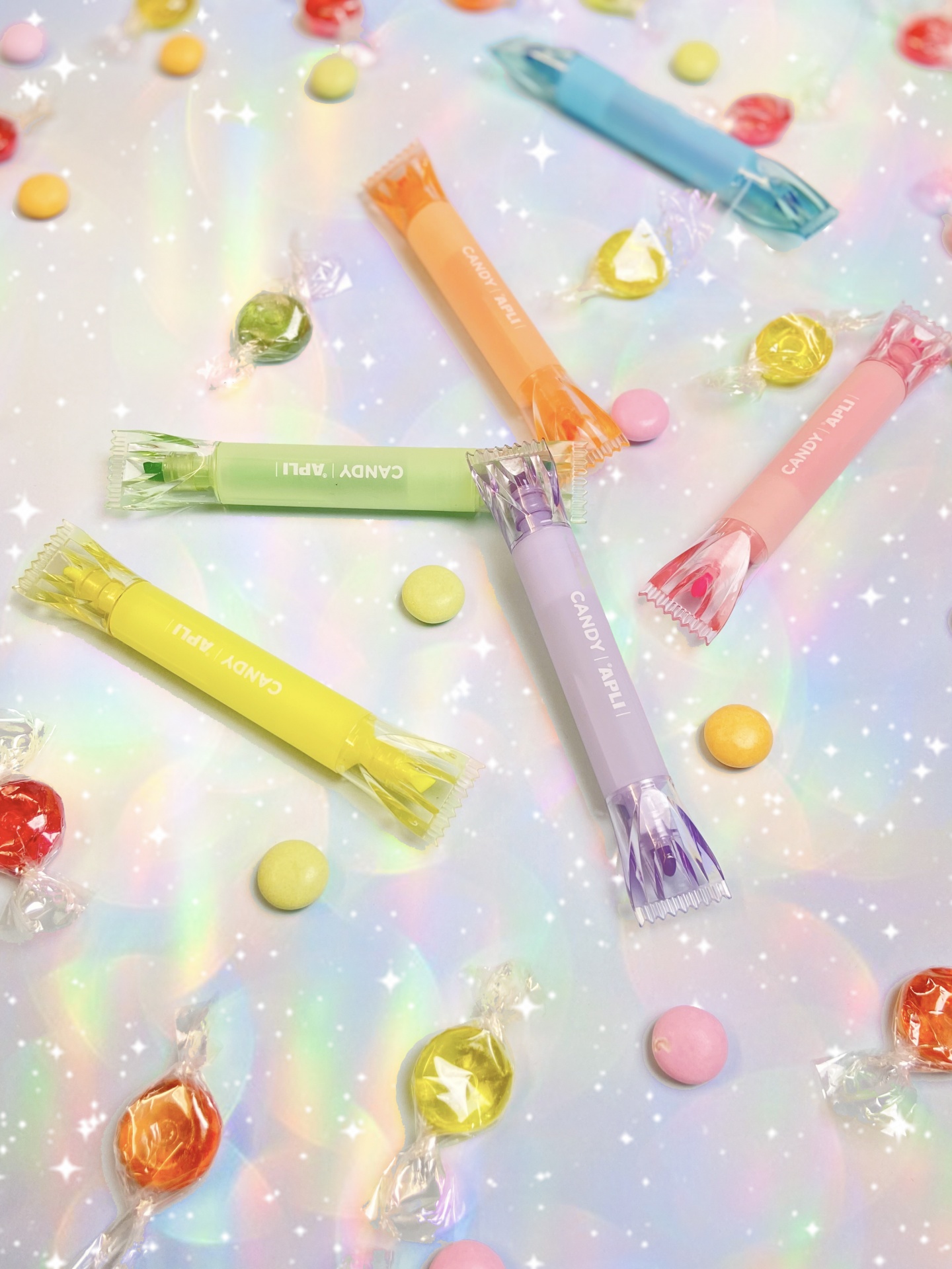 Doces coloridos em embalagens tubulares e redondas sobre superfície iridescente.