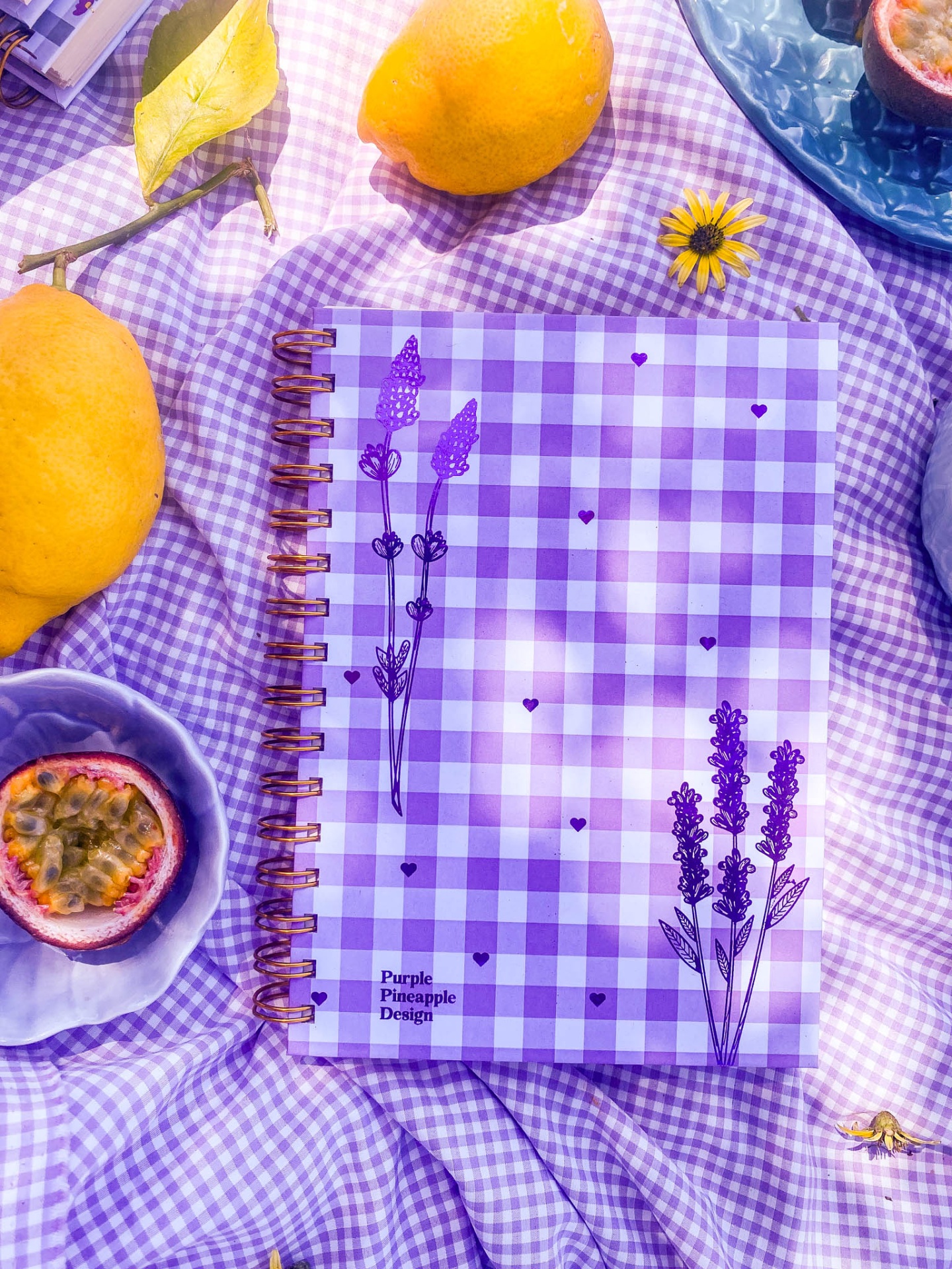 Caderno quadriculado lilás com flores desenhadas e espiral metálica sobre tecido lilás e frutas