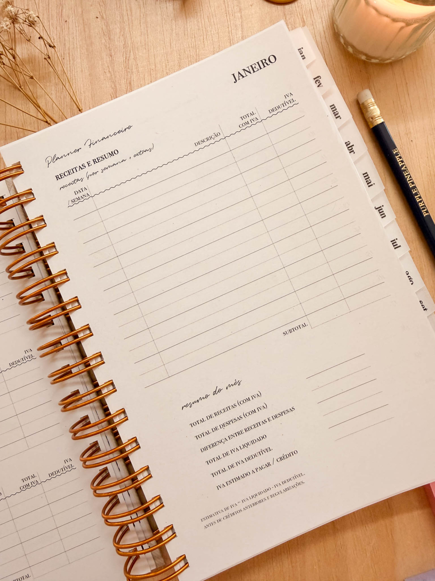 Planner financeiro com colunas para receitas e resumo, caneta preta e vela sobre mesa de madeira