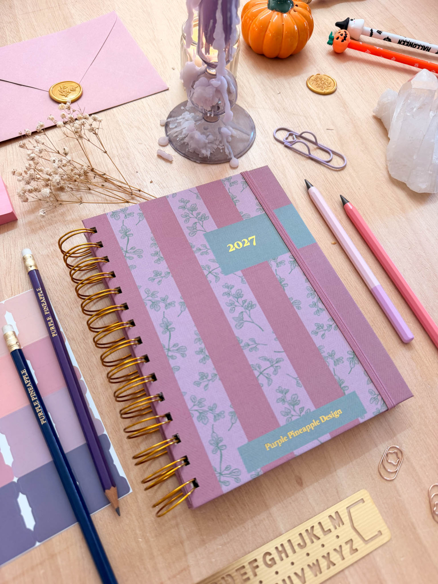 Agenda rosa e lilás com capa decorada sobre mesa com vários objetos