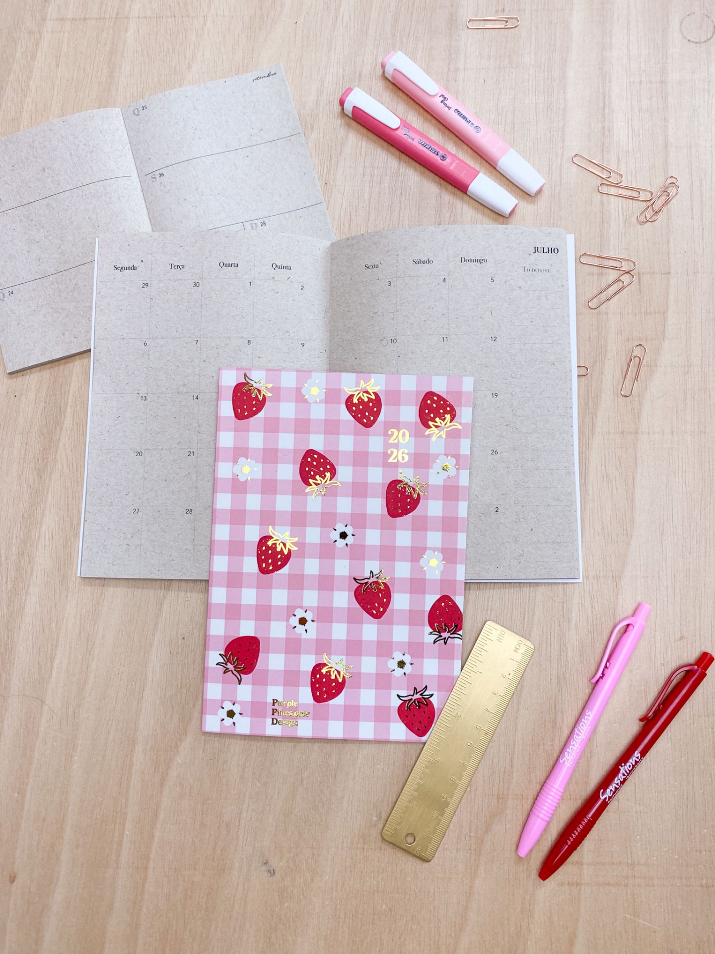 Agenda 2023 rosa com morangos, canetas e clips sobre mesa de madeira