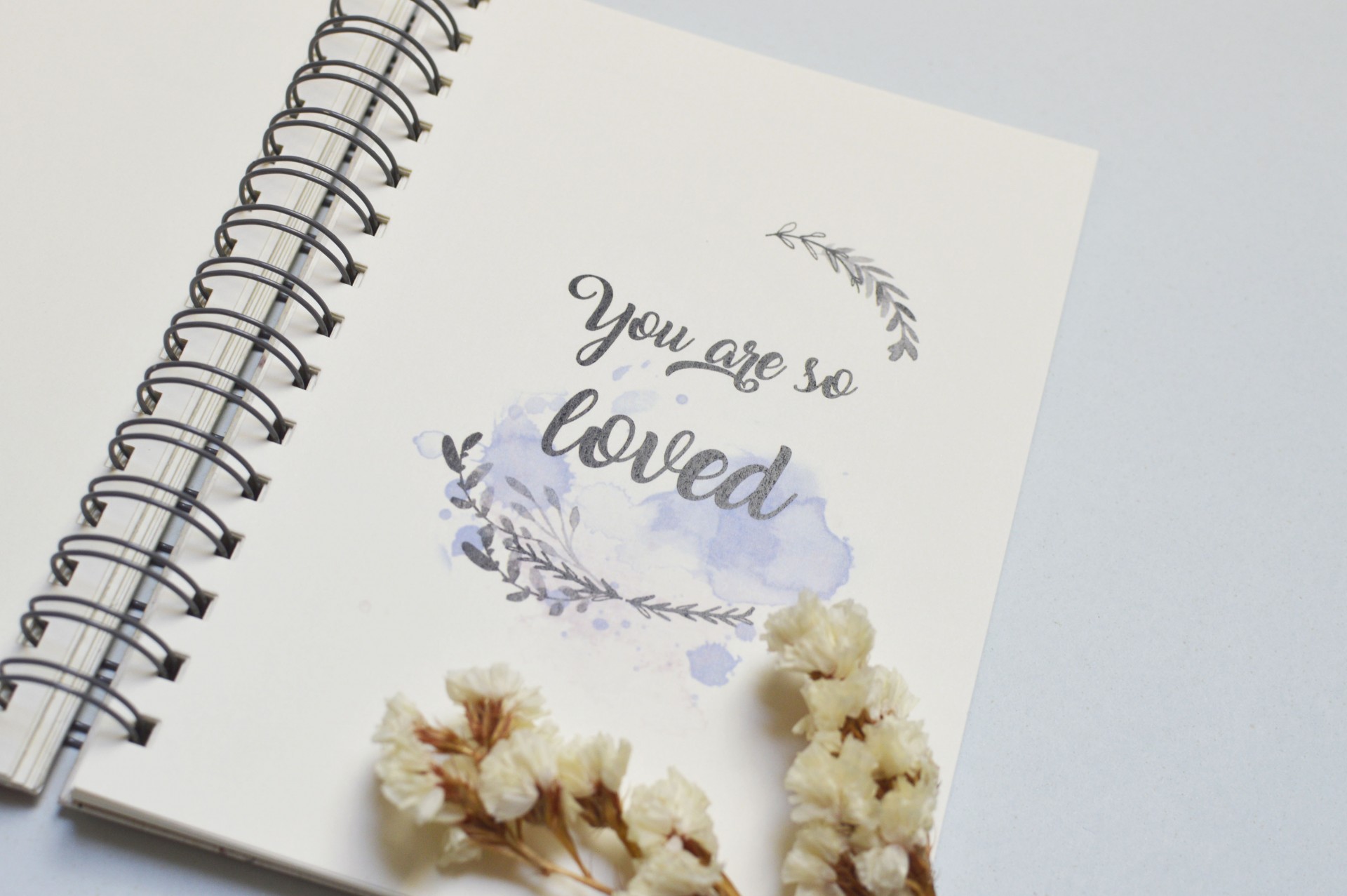 Caderno branco com texto decorativo e flores secas ao lado