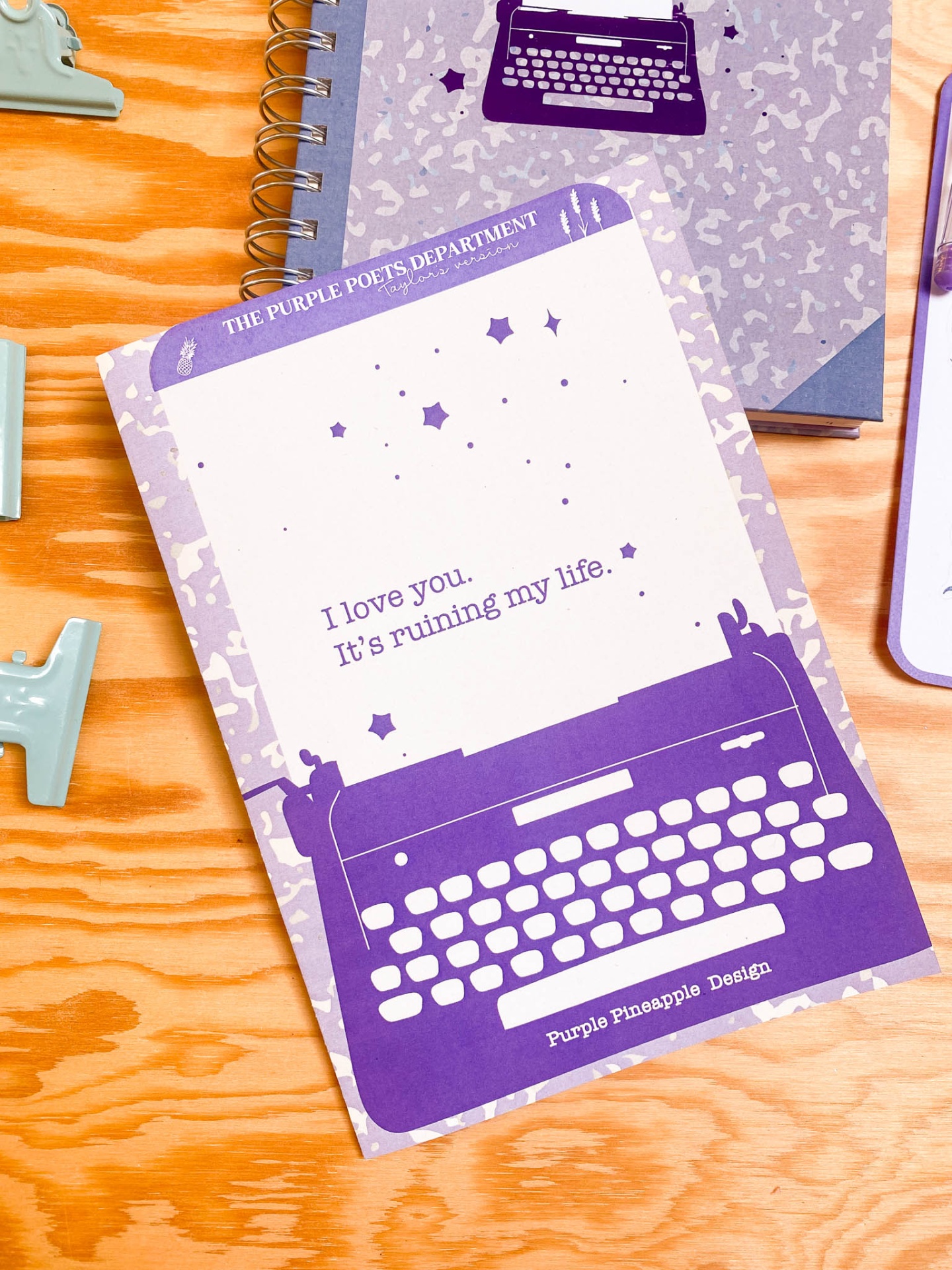 Caderno roxo com ilustração de máquina de escrever e texto sobre mesa de madeira