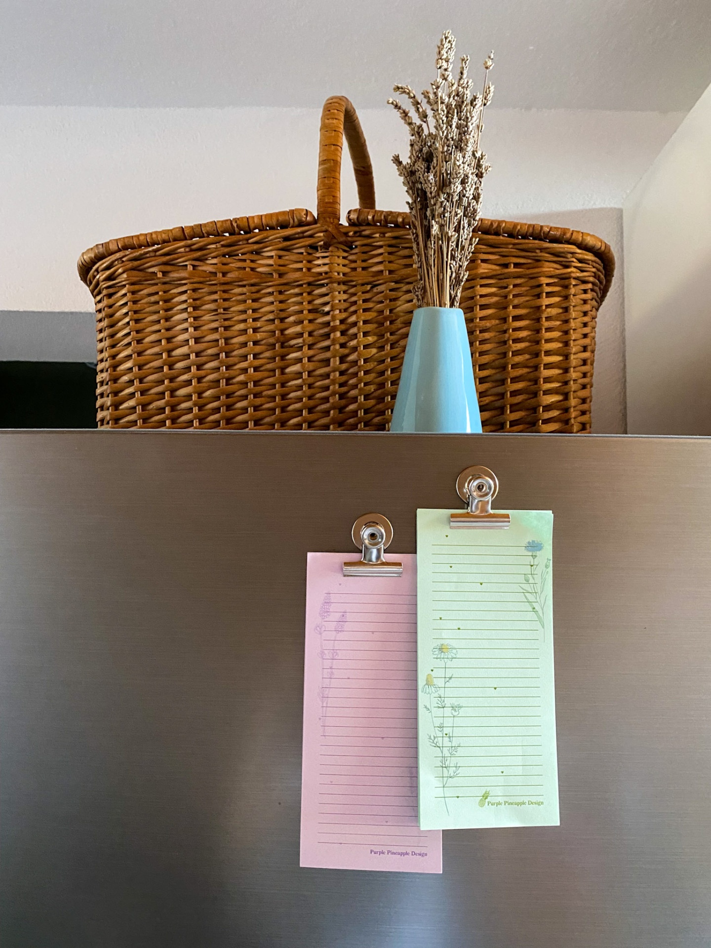 Cesta de verga com ramo seco em vaso e listas de papel presas num armário prateado