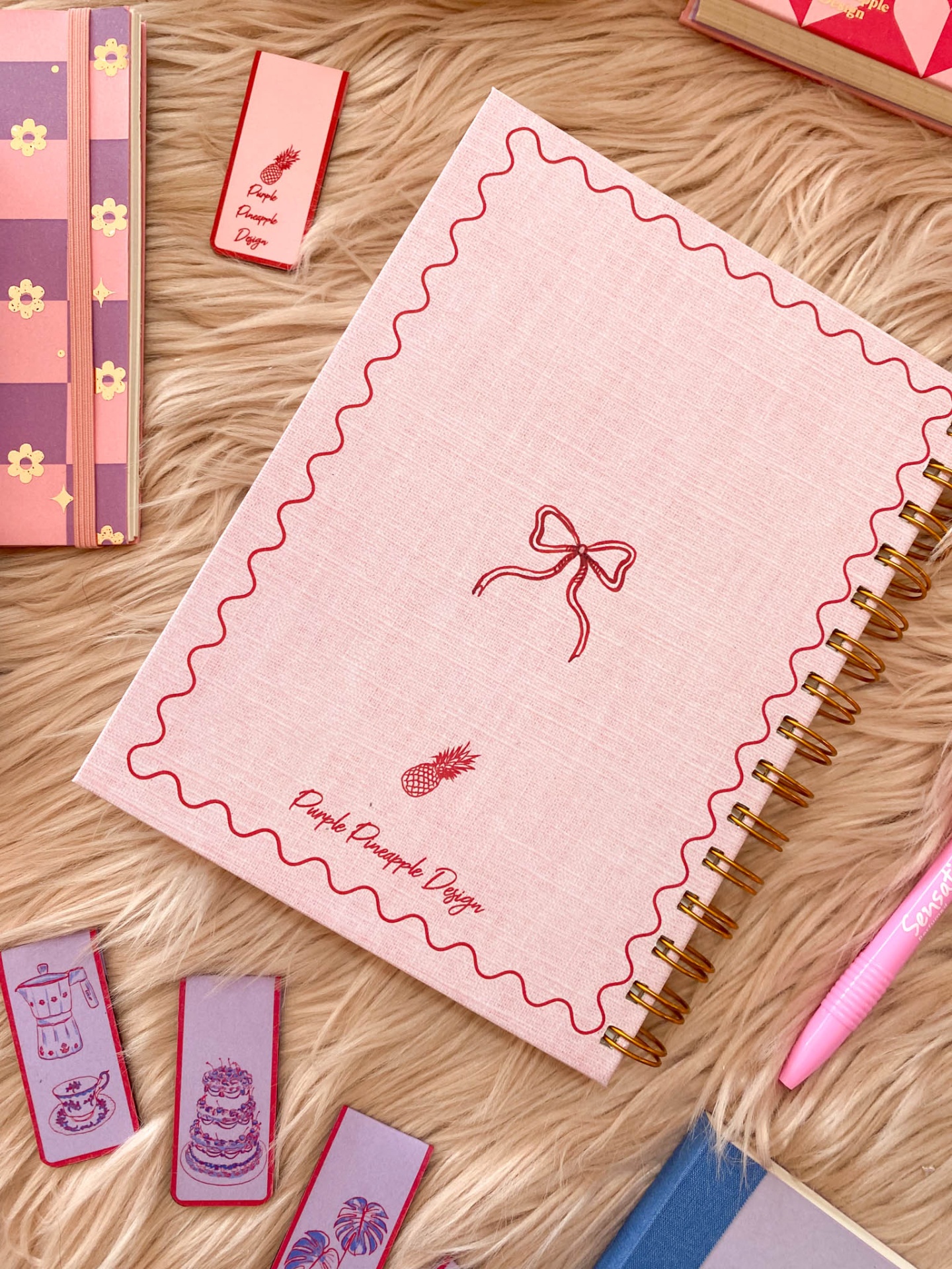 Caderno espiral rosa claro com design vermelho e clips decorativos coloridos sobre tapete de pêlo