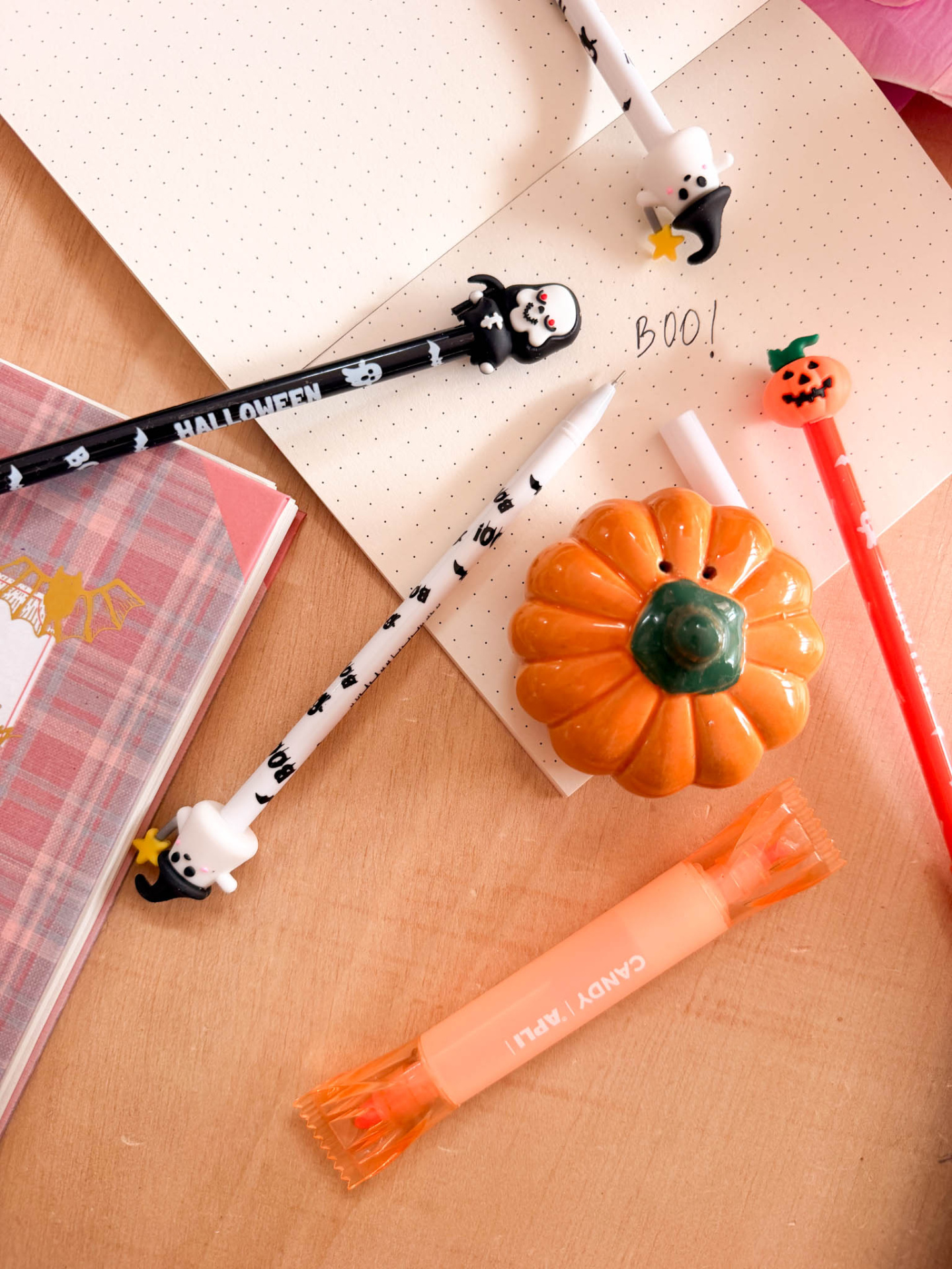 Canetas de Halloween com personagens decorativos sobre caderno pontilhado e mesa de madeira