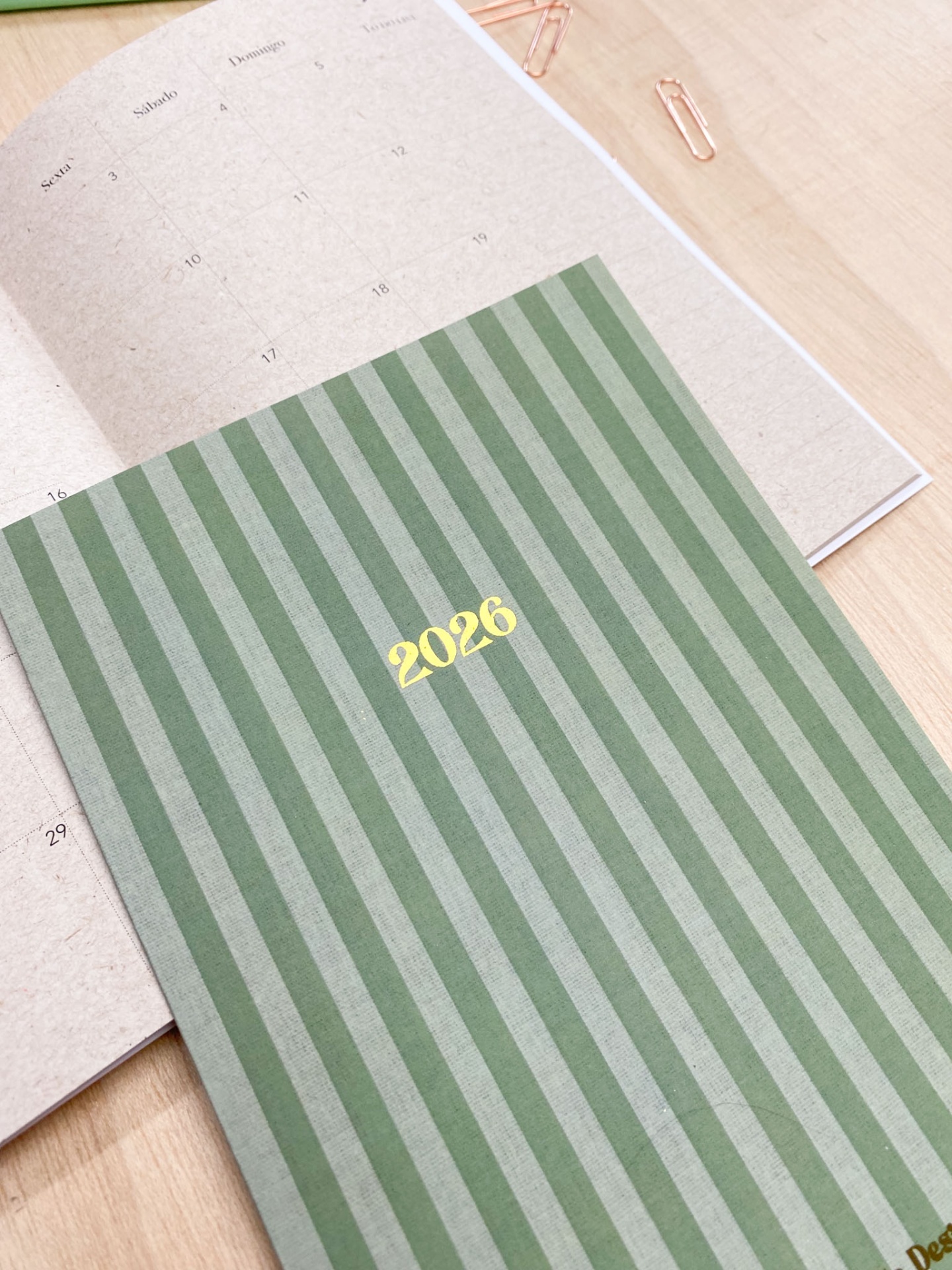 Agenda verde 2026 às riscas com calendário aberto em papel reciclado sobre mesa de madeira.