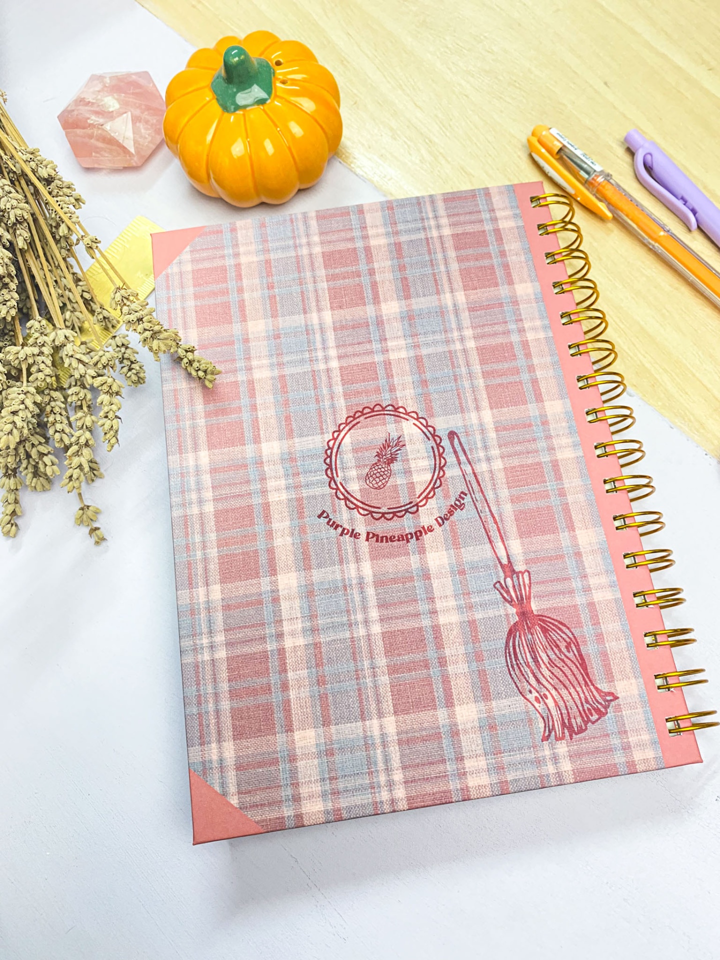 Caderno com capa xadrez rosa, padrão visual e objetos de escritório numa mesa.