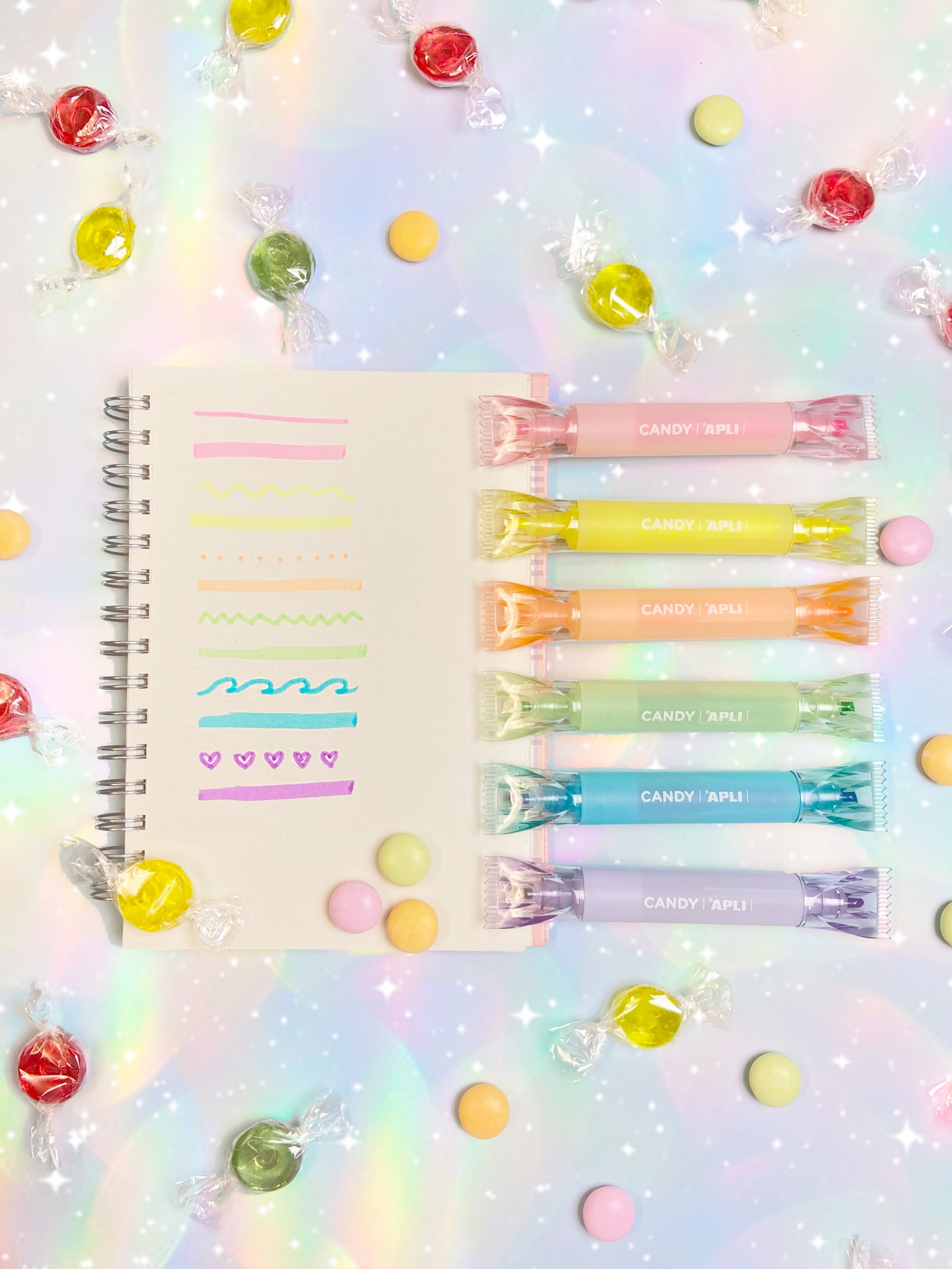 Bloco de notas com canetas coloridas e rebuçados sobre fundo holográfico