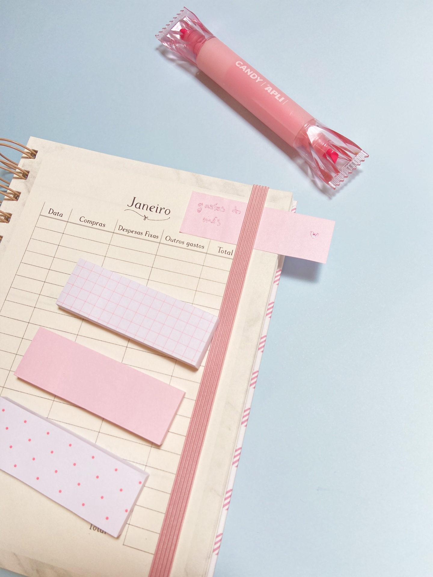 Caderno aberto de controlo de despesas com notas autocolantes rosa e doce embalado rosa em fundo azul claro