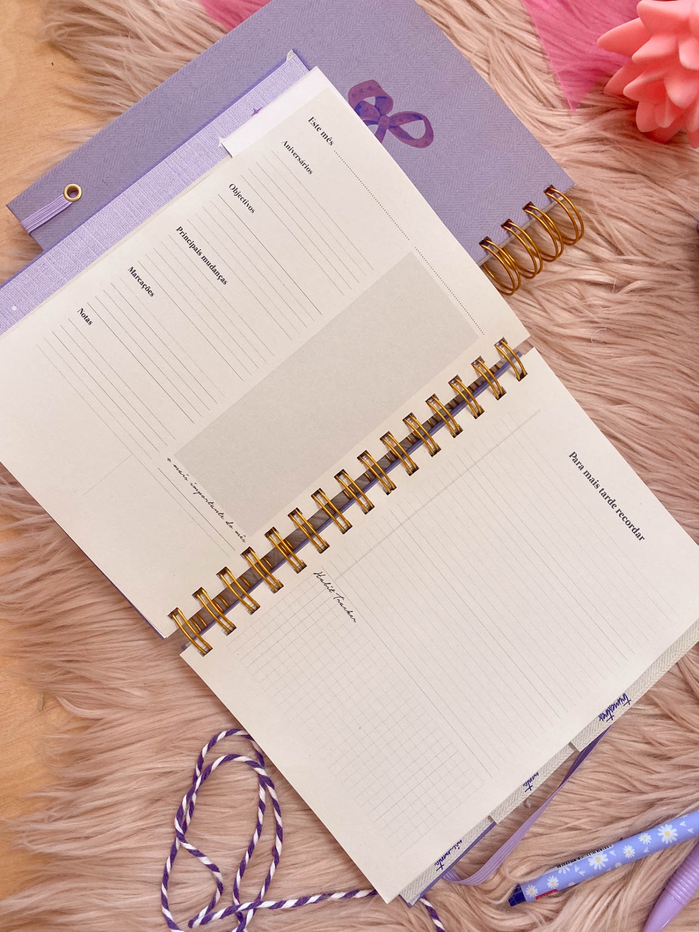 Bloco de notas espiral lilás aberto sobre tecido felpudo rosa com lápis e fita roxa