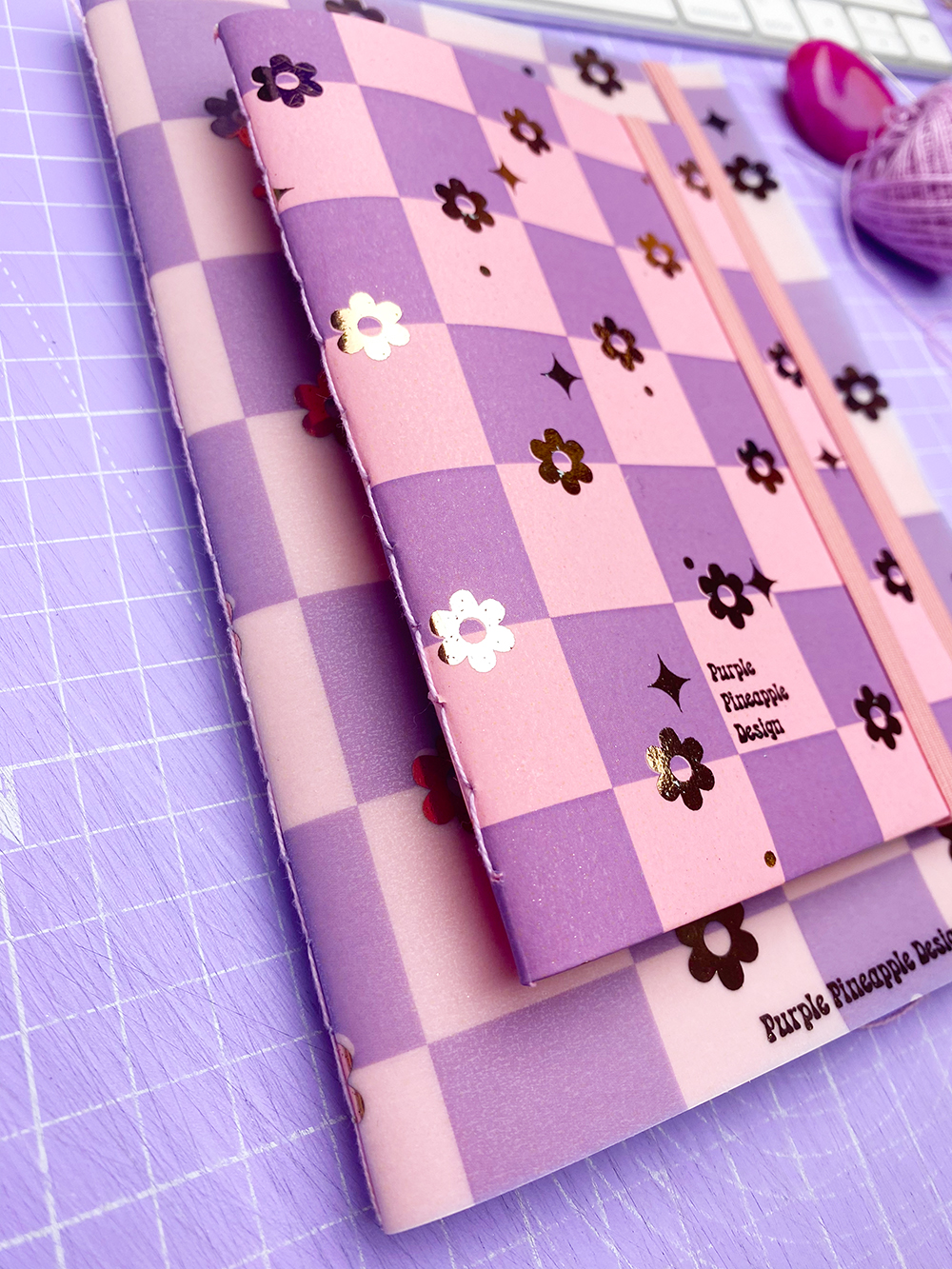 Cadernos com capas xadrez rosa e roxa com flores metálicas e texto Purple Pineapple Designs