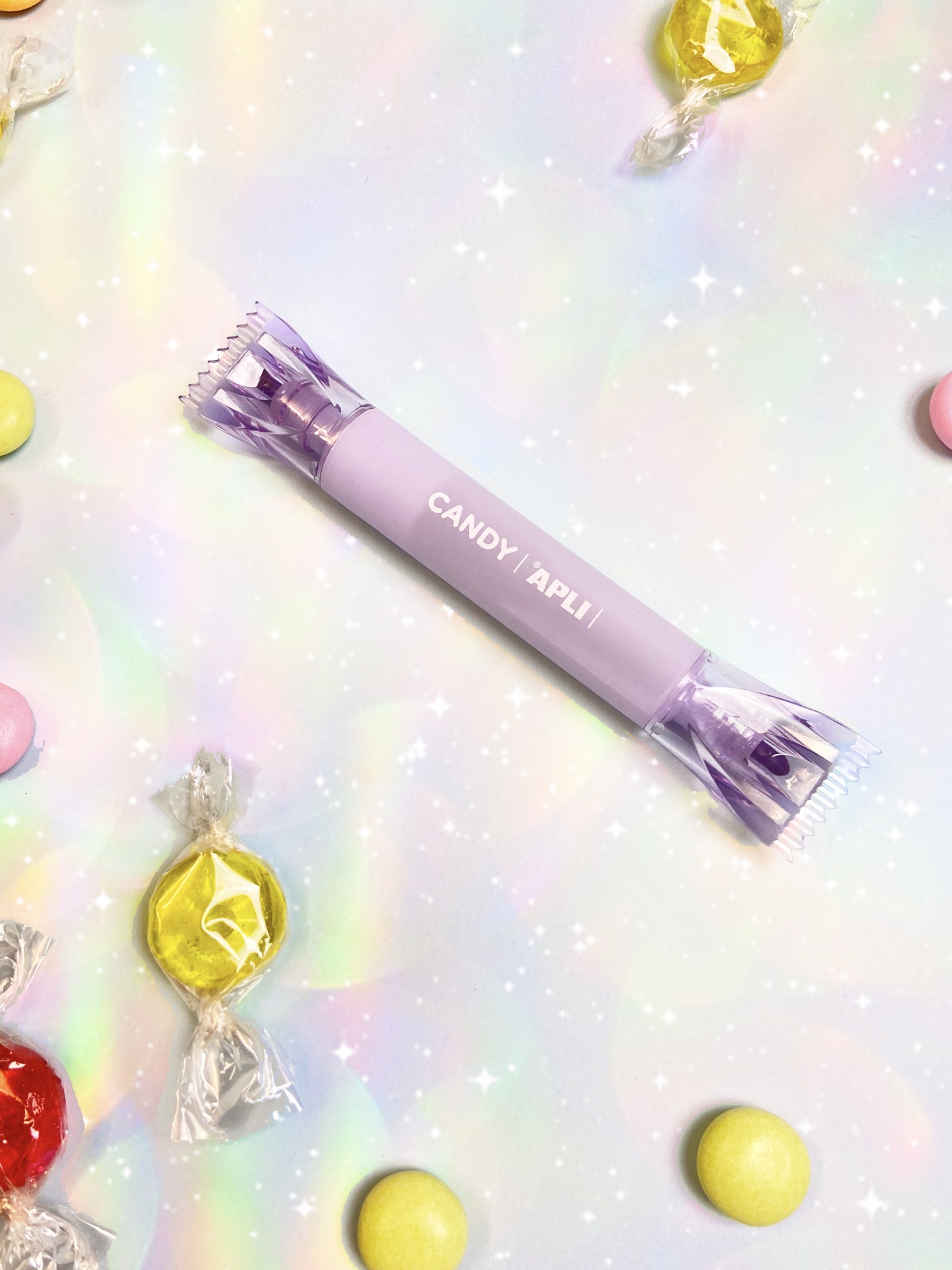 Doce embrulhado roxo com texto CANDY | APLI rodeado de balas coloridas e superfície cintilante