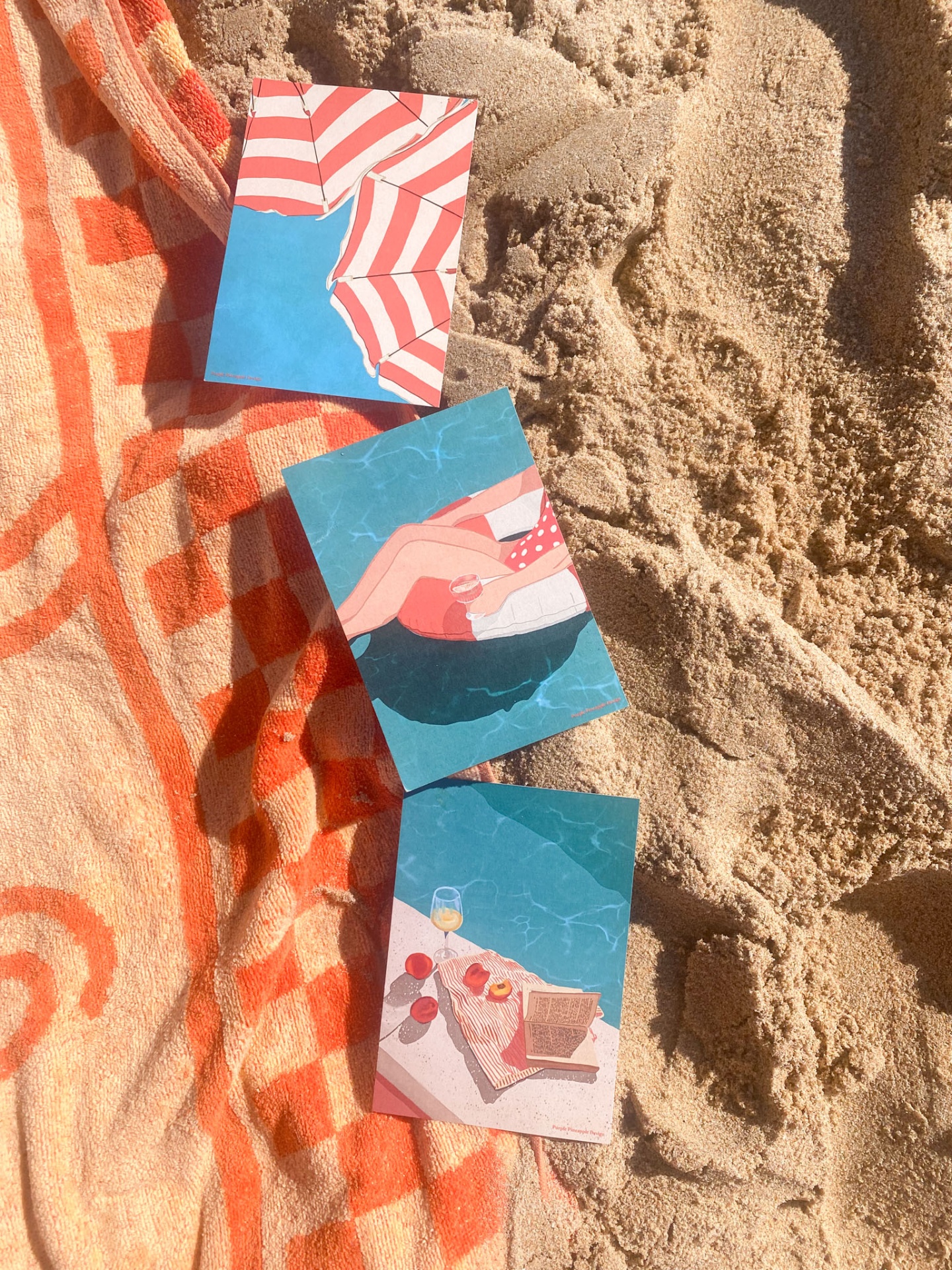 Três cartões com ilustrações de praia sobre toalha laranja na areia