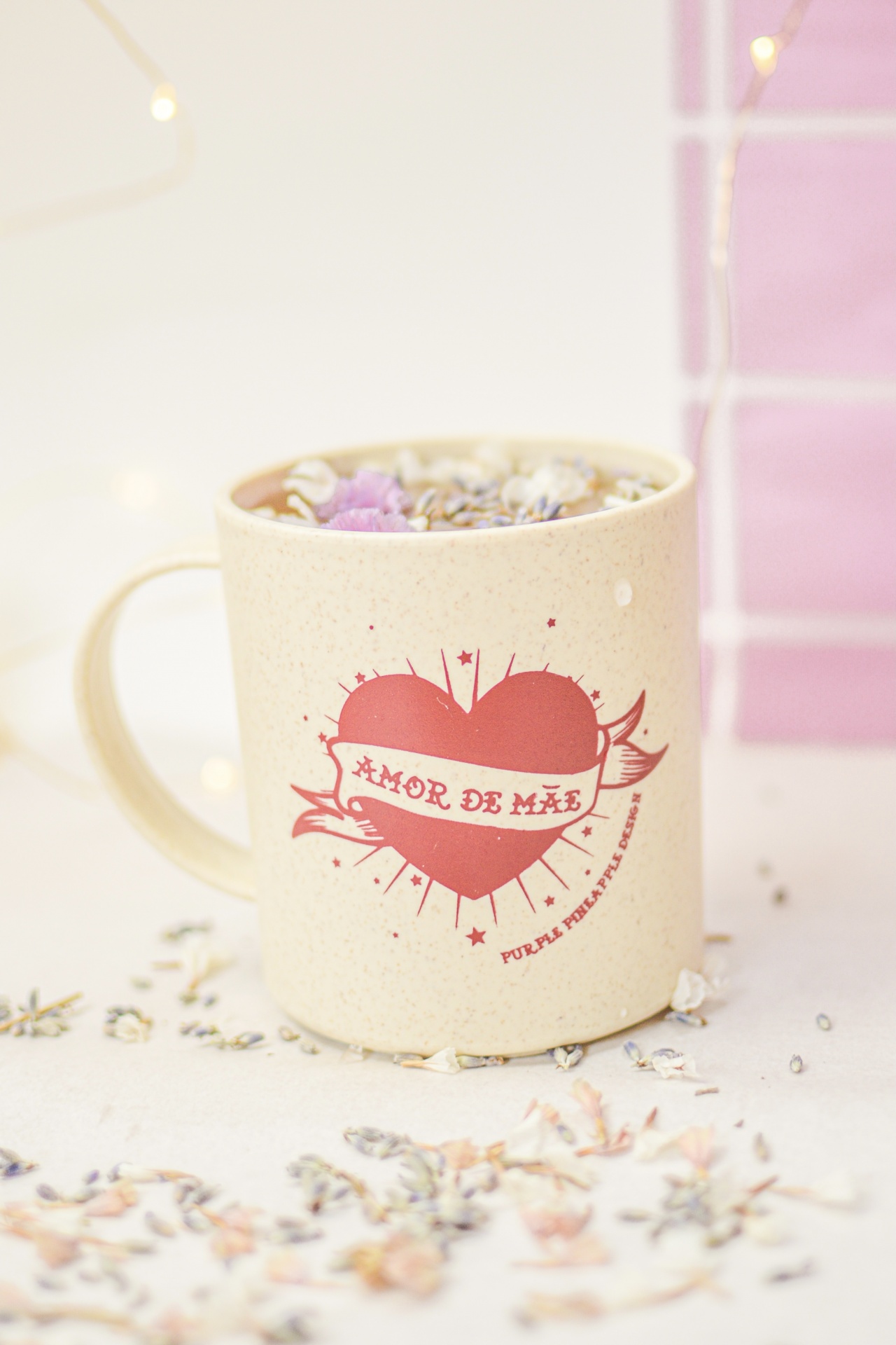 Caneca bege com coração vermelho e frase Amor de Mãe, bebida quente com flores secas encima