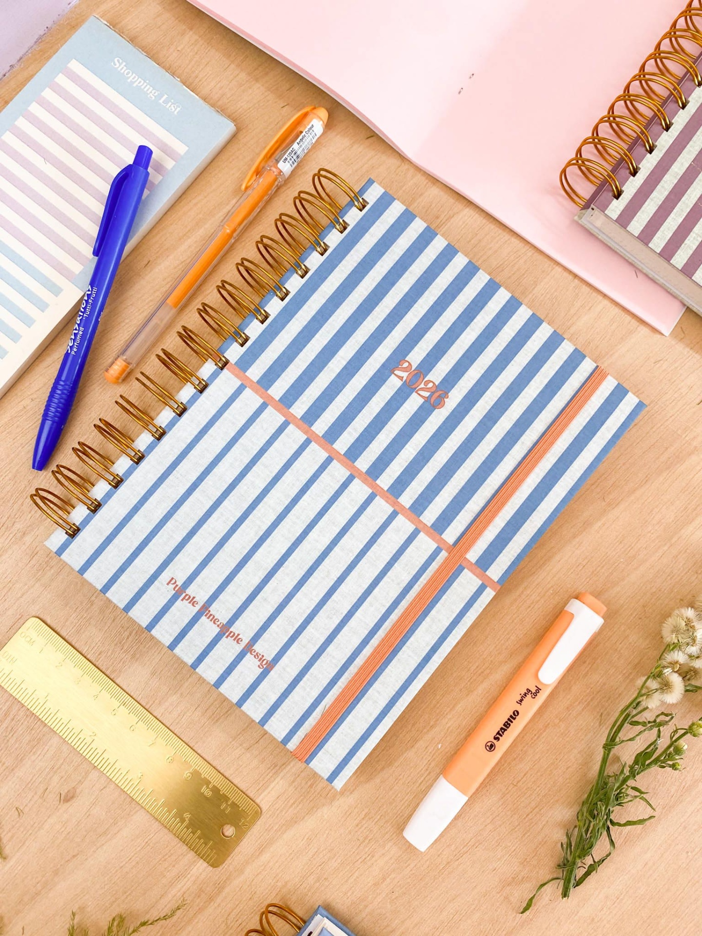 Caderno riscado azul claro e branco com canetas e régua numa mesa de madeira clara