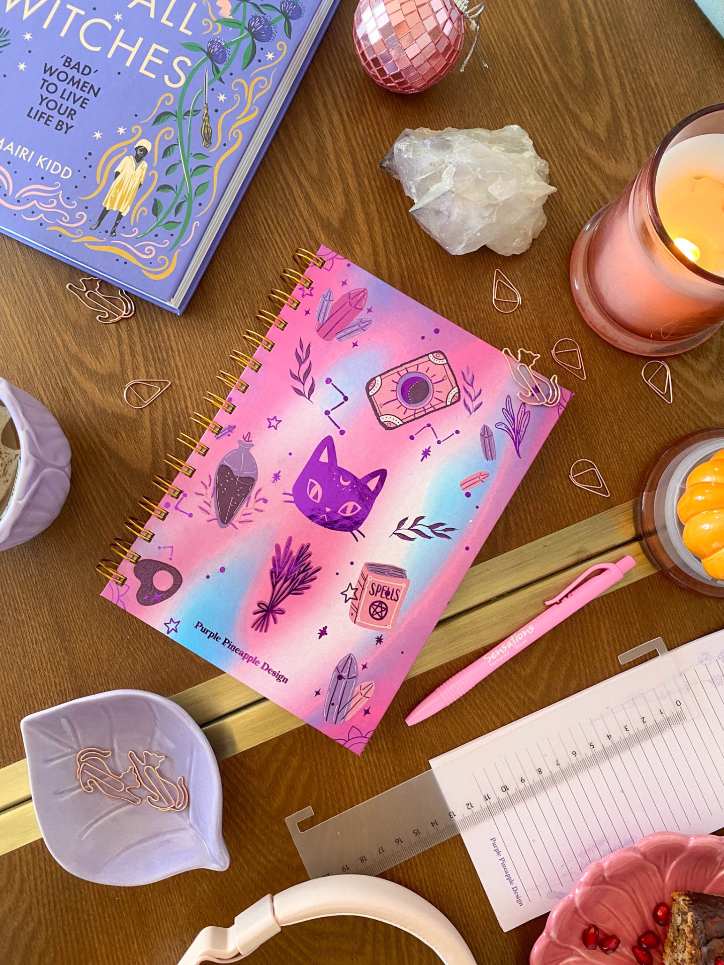 Agenda espiral decorada sobre mesa de madeira com objetos variados ao redor