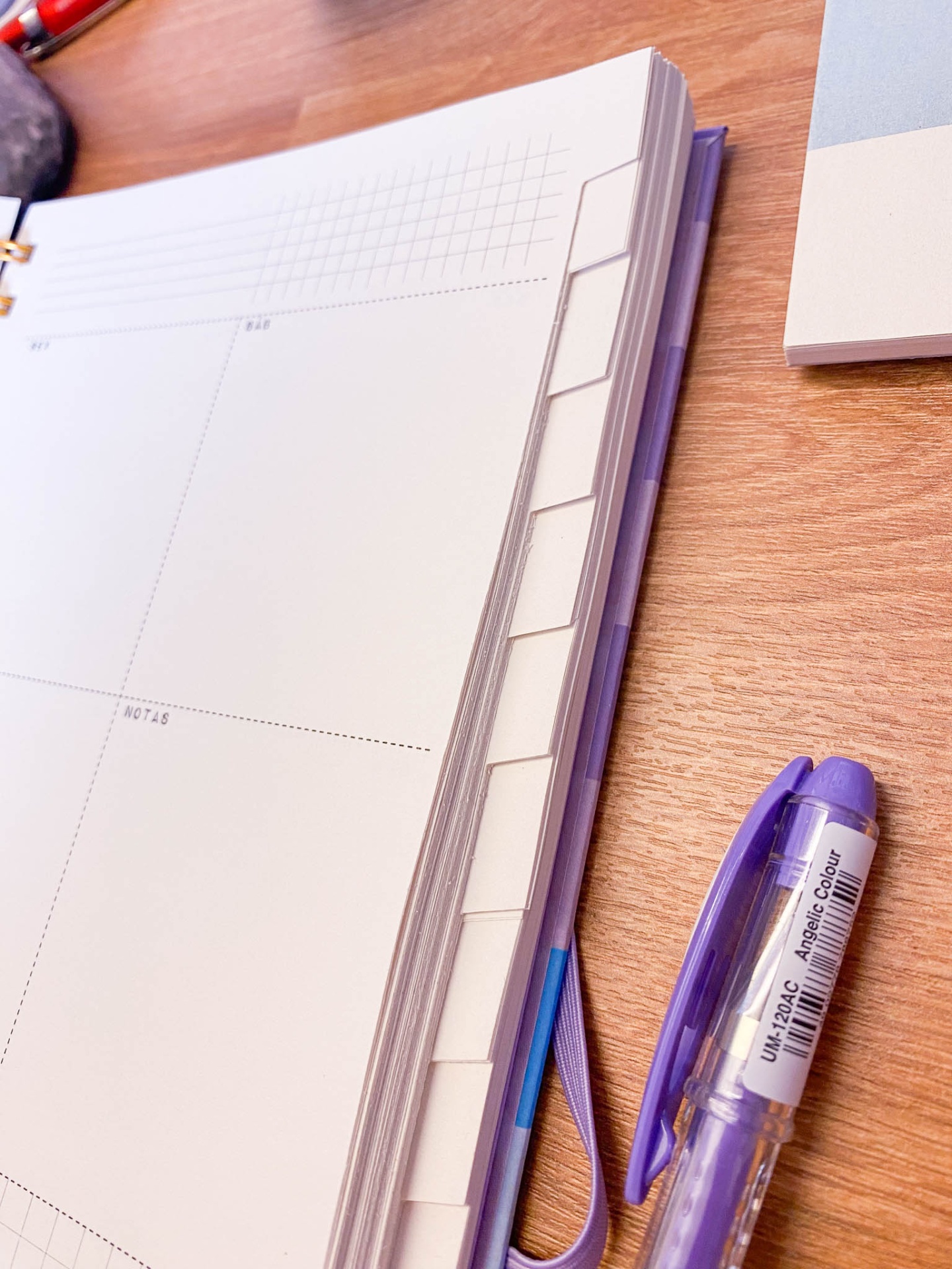 Agenda com abas e caneta roxa sobre mesa de madeira