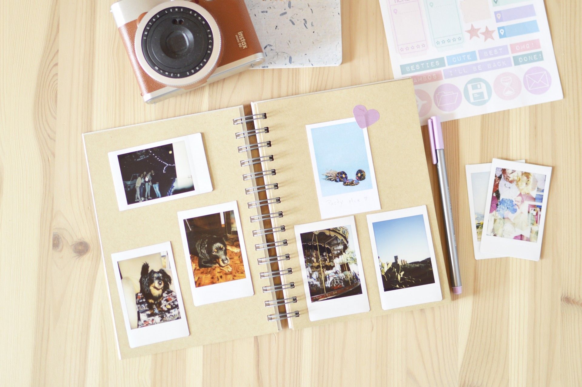 Agenda espiral com fotografias instantâneas, caneta, autocolantes e câmara instantânea sobre mesa